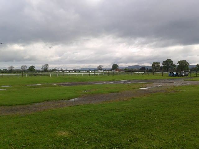 The course at Thirsk under a heavy grey sky, standing water on the turf in front of the rail