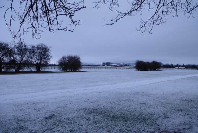 Thirsk Racecourse under a covering of winter snow, bare trees along the far rail