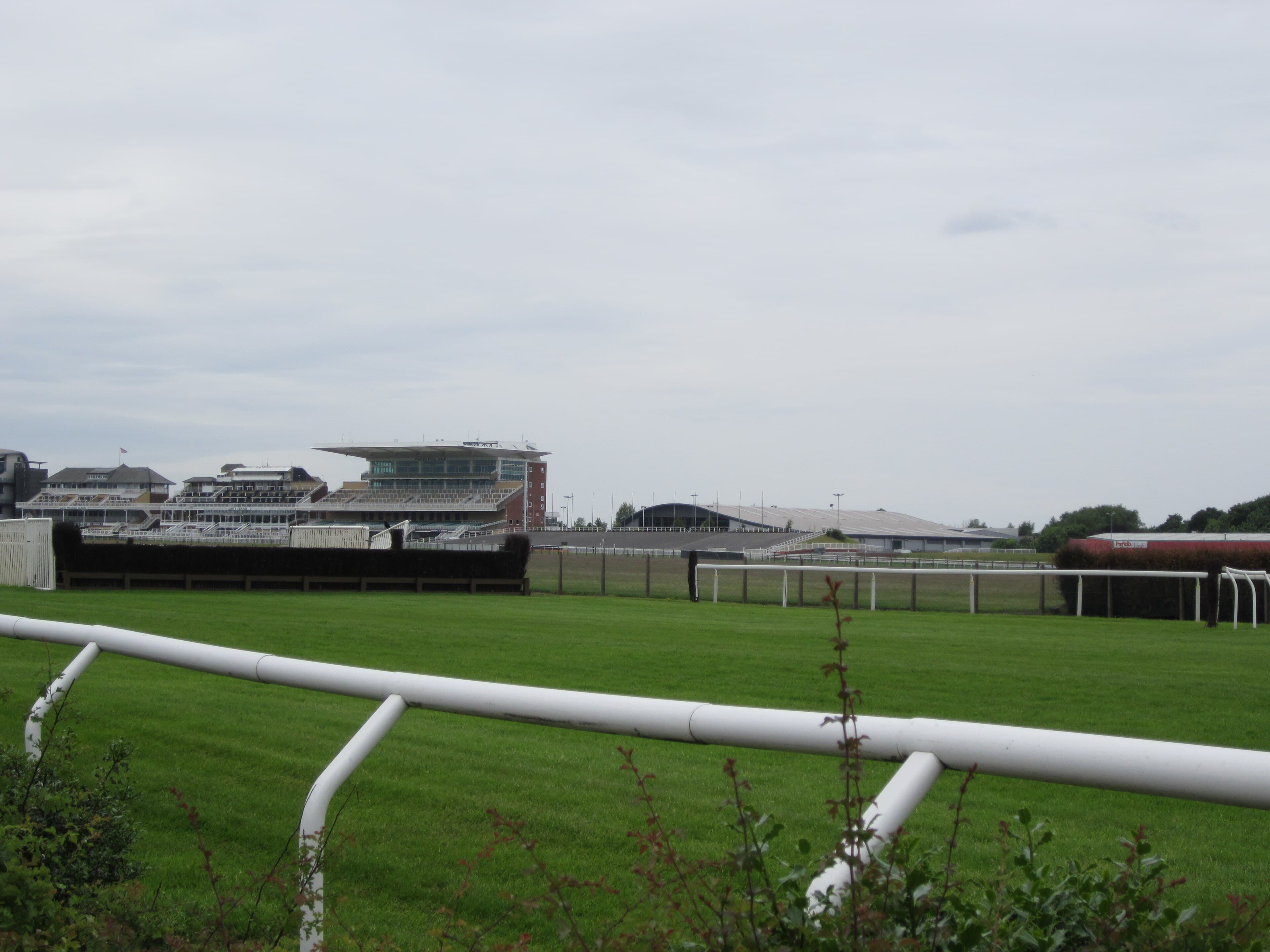 The white running rail curving away across the Aintree turf, with a National fence and the grandstands in the distance.