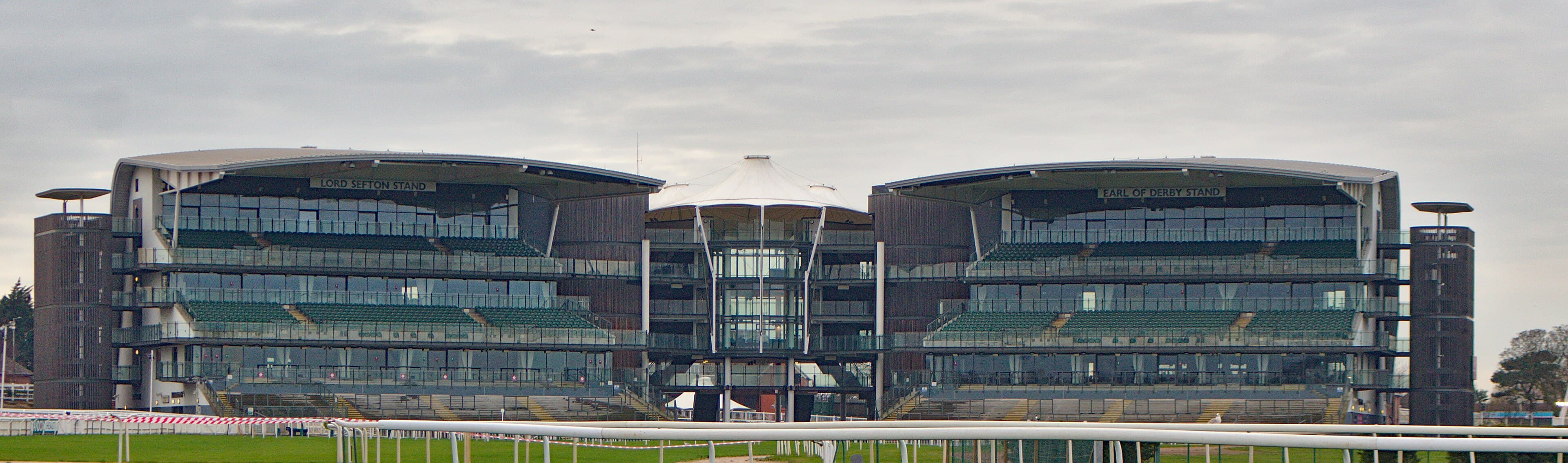 The Lord Sefton and Earl of Derby stands at Aintree seen across the running rail on a grey winter day.
