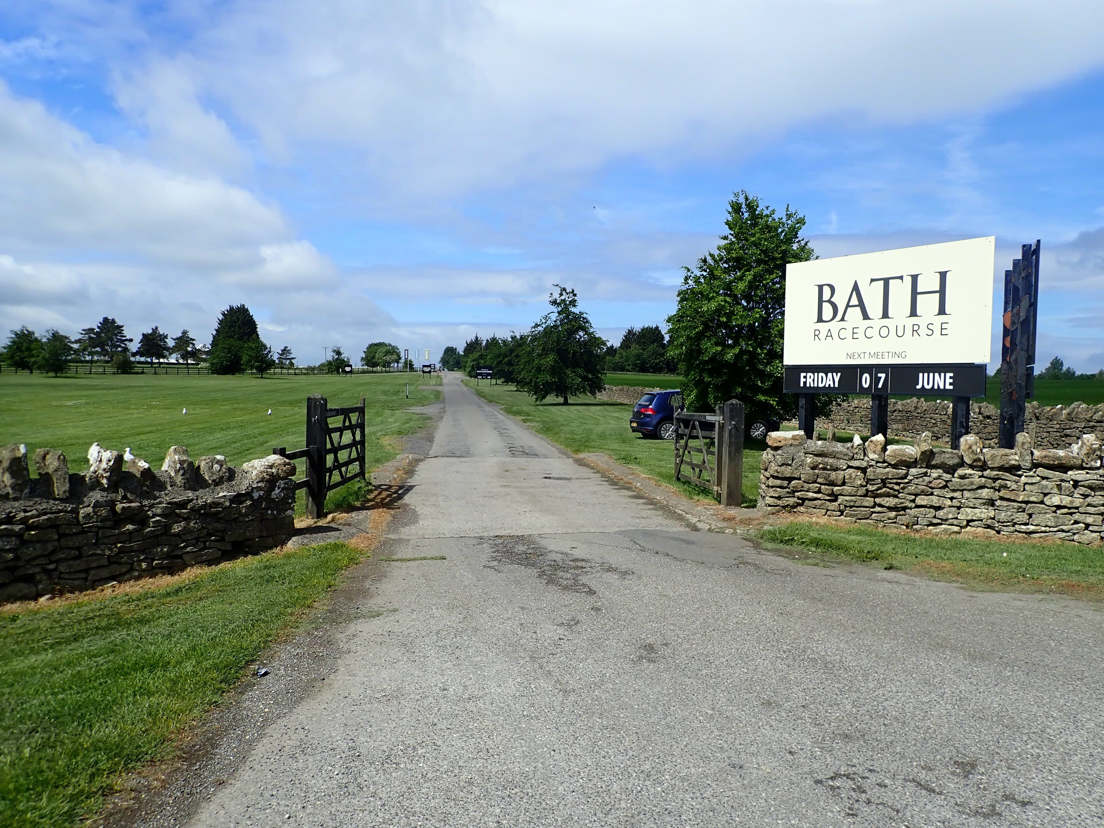 The Bath Racecourse board at the entrance drive, the dry stone wall and the course beyond it.