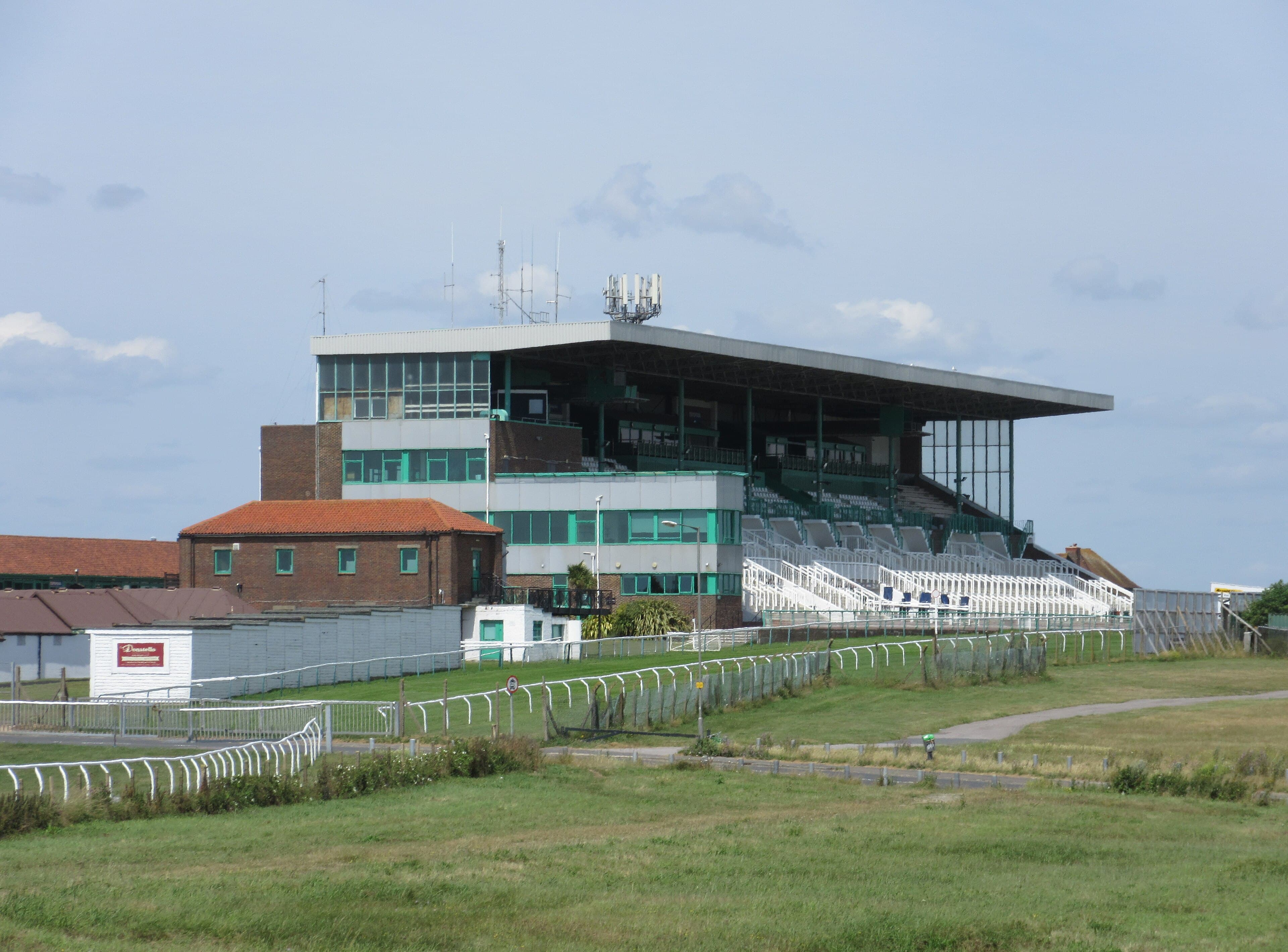 The green and white grandstand at Brighton racecourse above the rails on Whitehawk Hill.