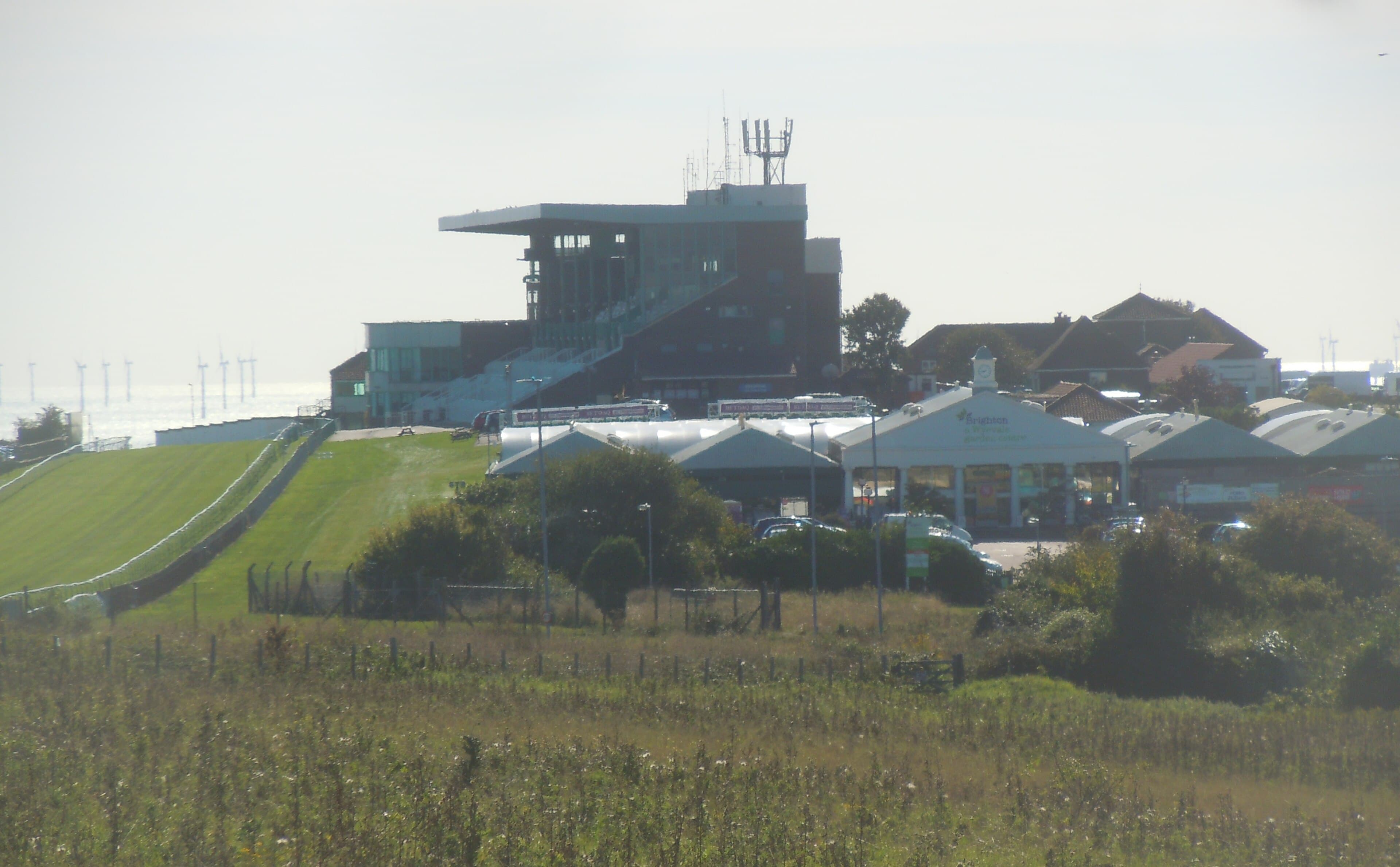 The Brighton stand seen across rough grass, the sea and a wind farm behind it.