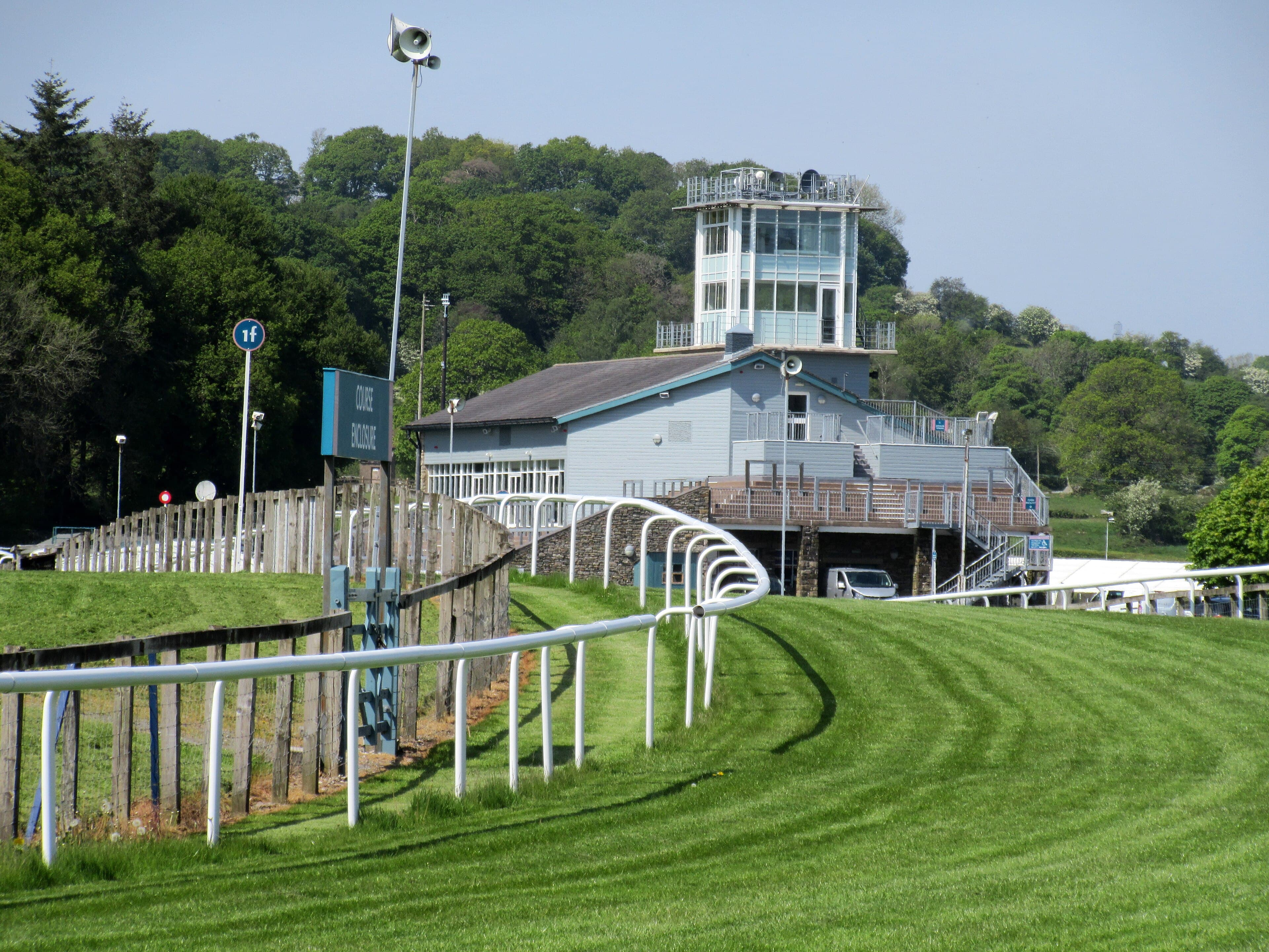 The judge's box and course enclosure stand at Cartmel above the bend, backed by the hillside wood.