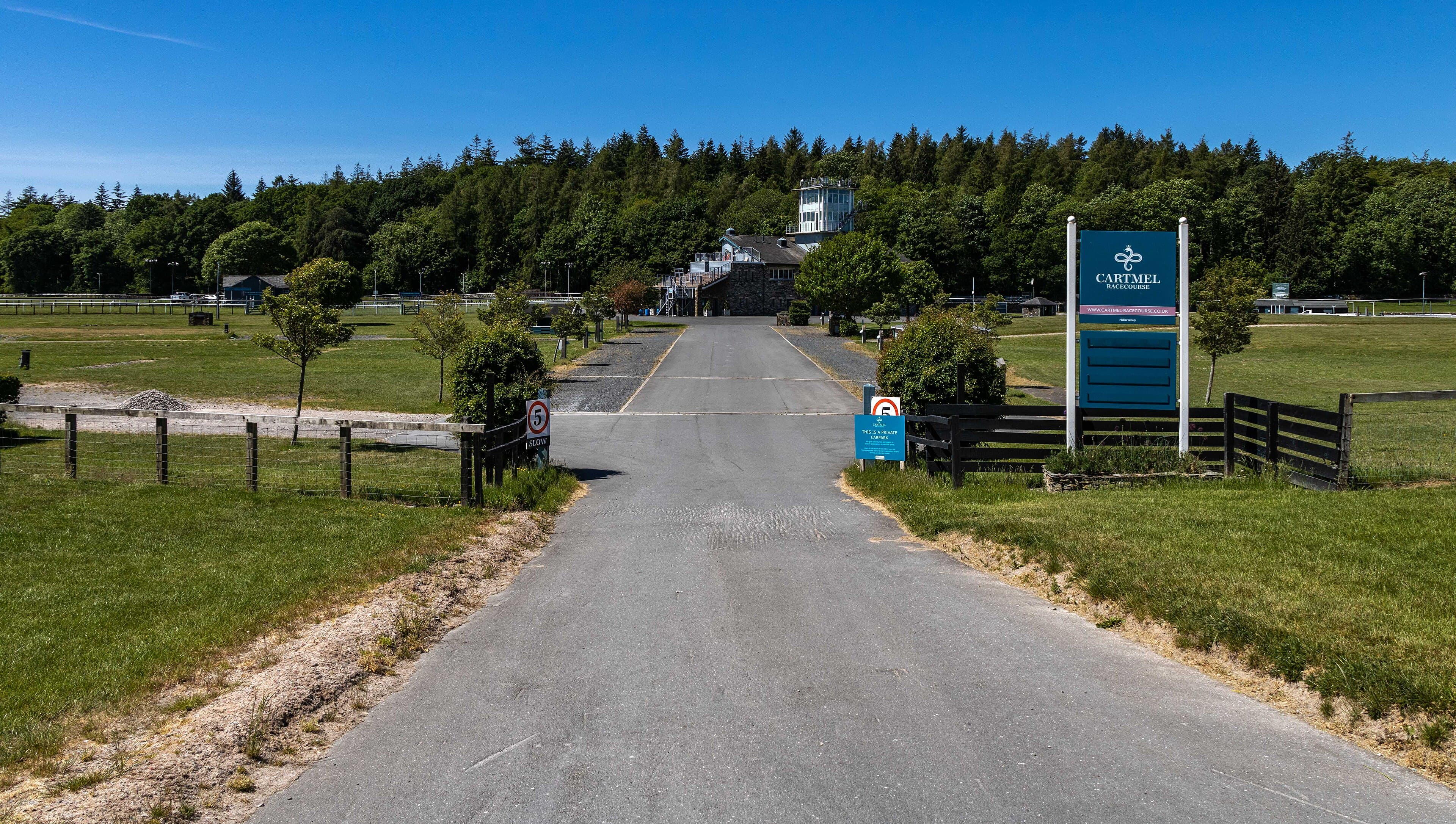 The Cartmel Racecourse sign at the head of the drive, the stand and the woods behind.