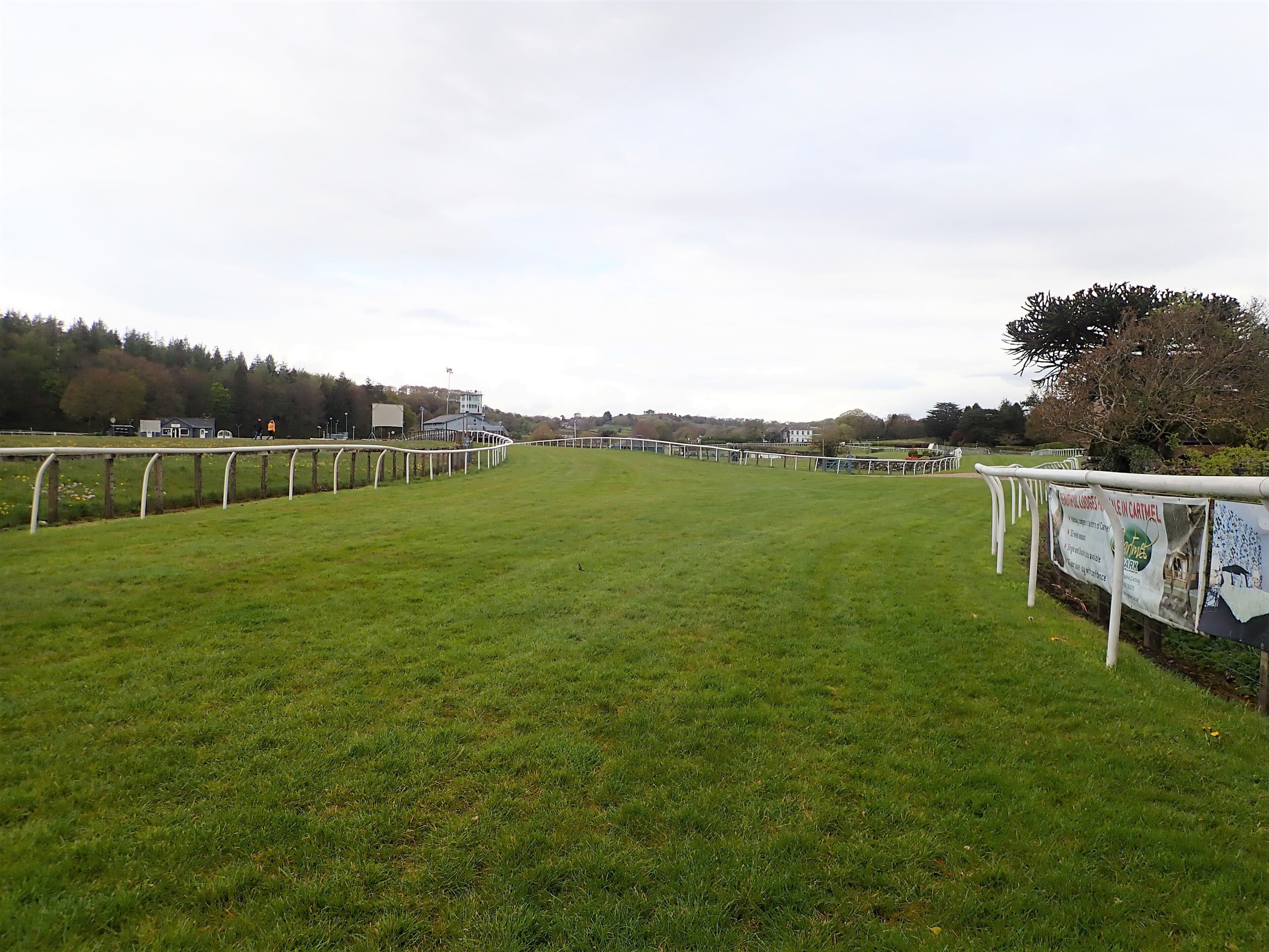The long straight at Cartmel in autumn, sponsor banners hanging along the far rail.