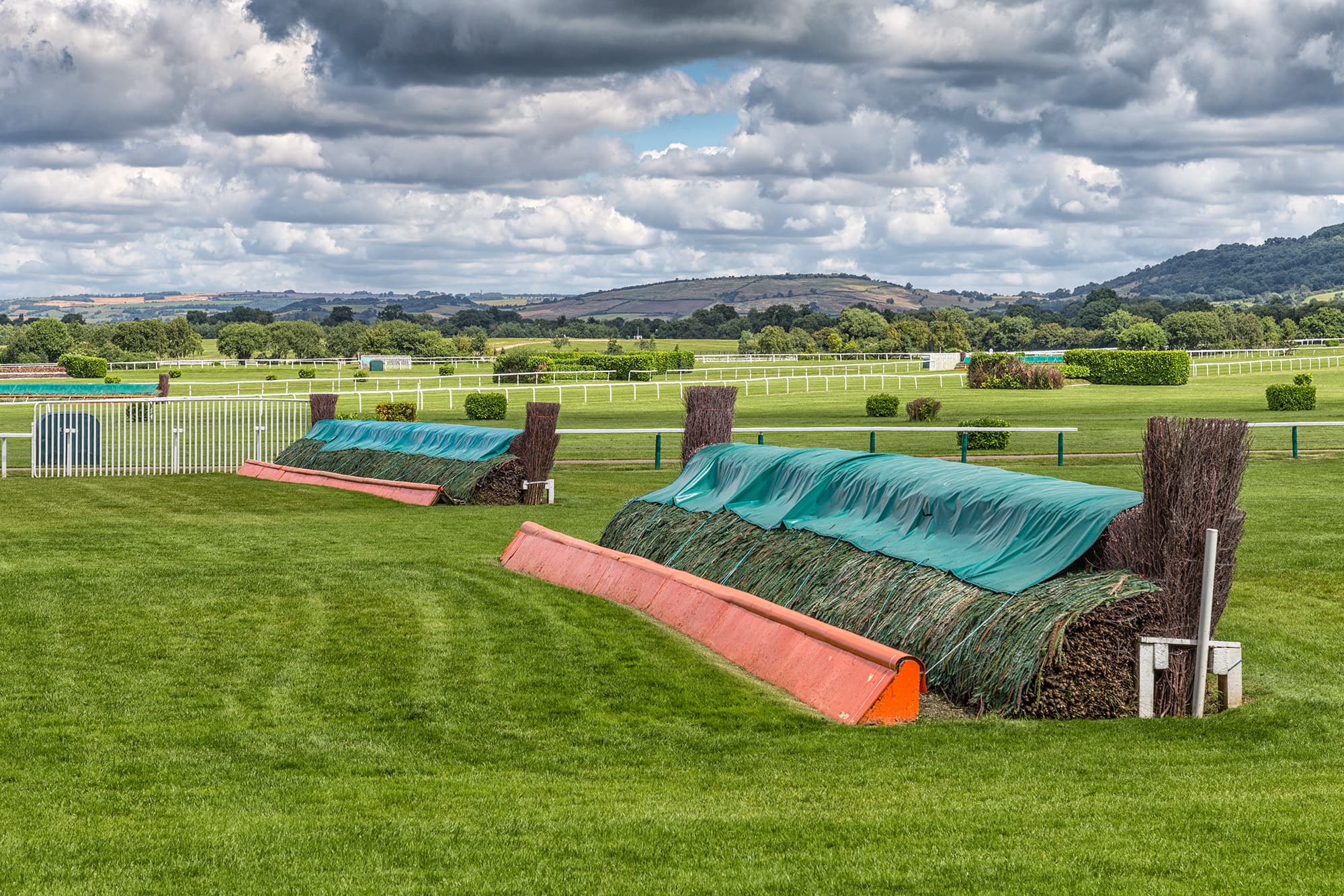 Two birch steeplechase fences under summer covers at Cheltenham, Cleeve Hill beyond.