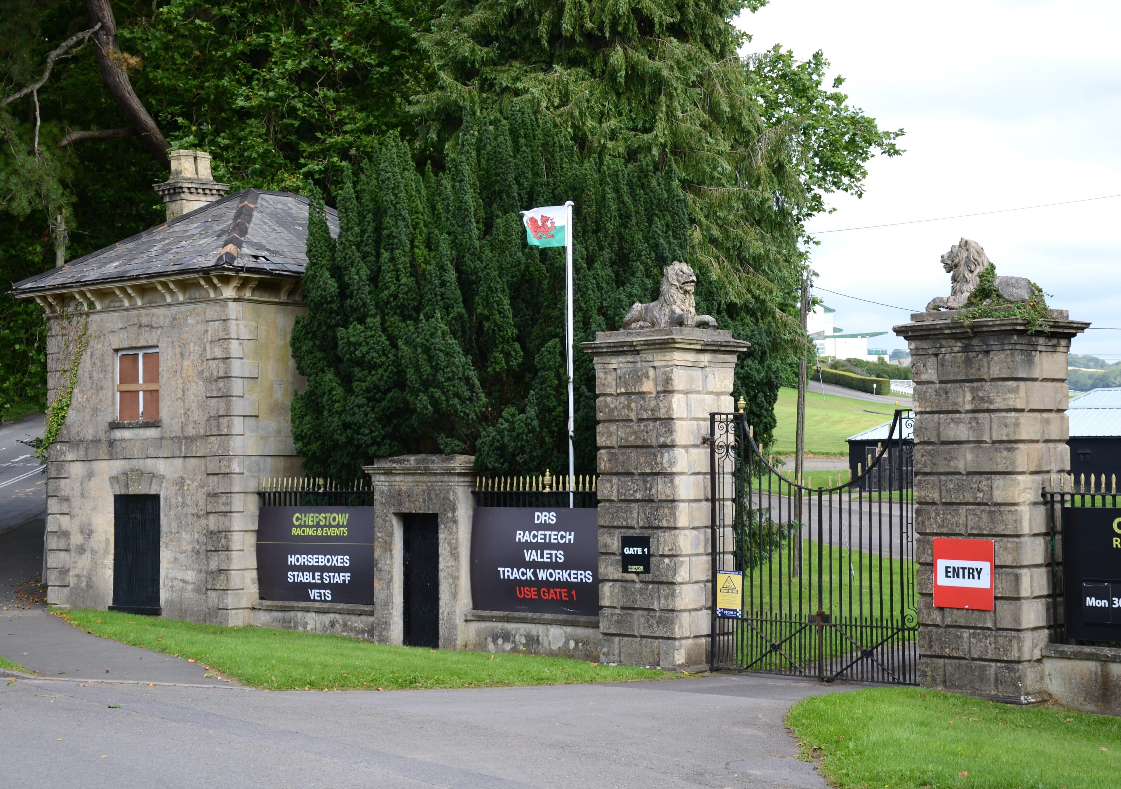 The stone lion gates and gate lodge at the entrance to Chepstow racecourse, a Welsh flag flying behind them.
