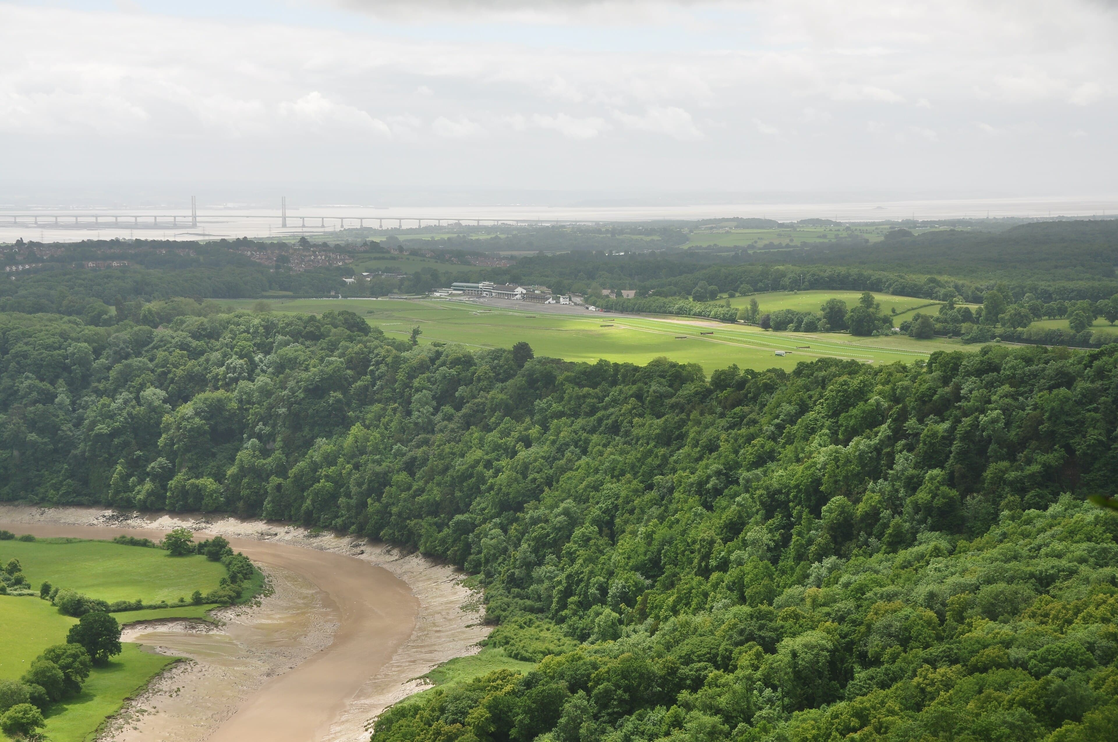 Chepstow racecourse seen from the Wyndcliff, the green oval of the track laid out beside the wooded gorge of the Wye with the Severn bridges beyond.