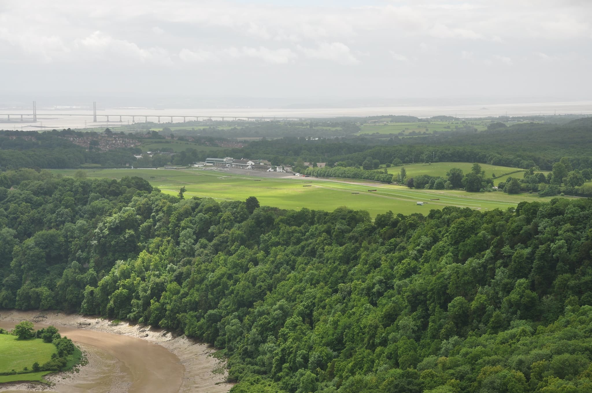 A high view over Chepstow racecourse from the Wyndcliff, with the River Wye curling round the wooded cliff below.
