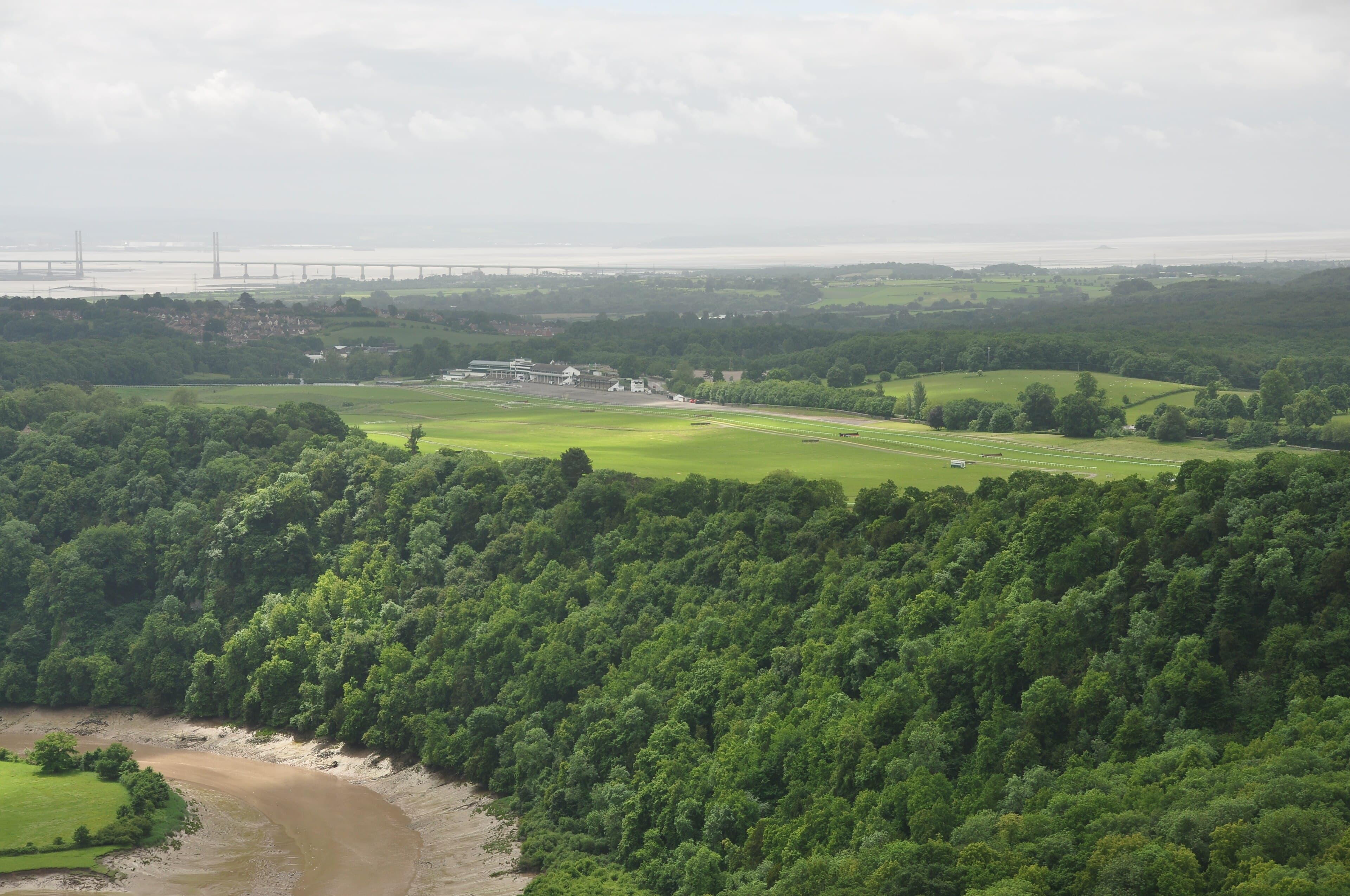 A high view over Chepstow racecourse from the Wyndcliff, with the River Wye curling round the wooded cliff below.