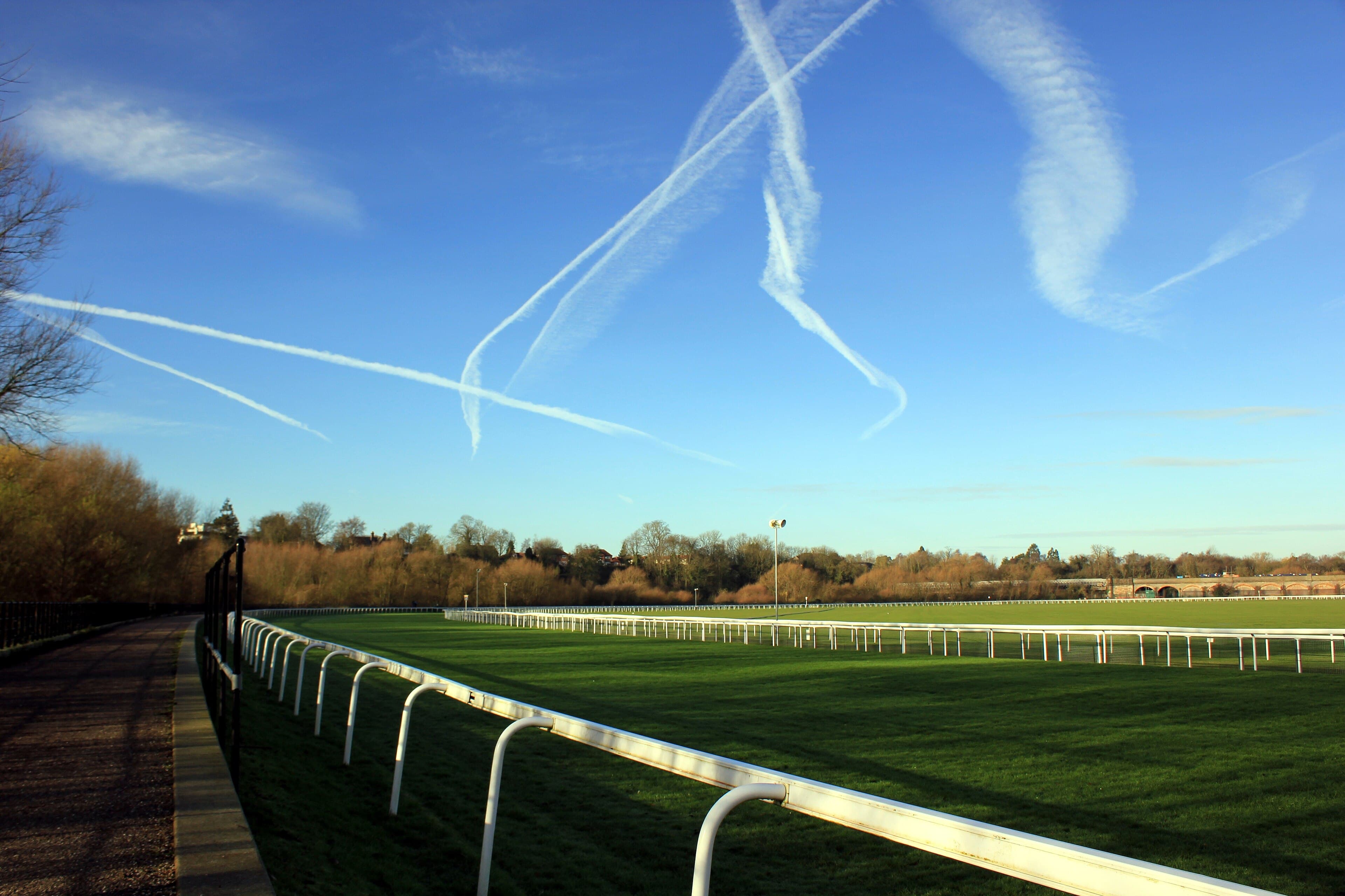 The running rail at Chester curving away under a blue winter sky, with bare trees on one side and the railway viaduct crossing the far end of the course.