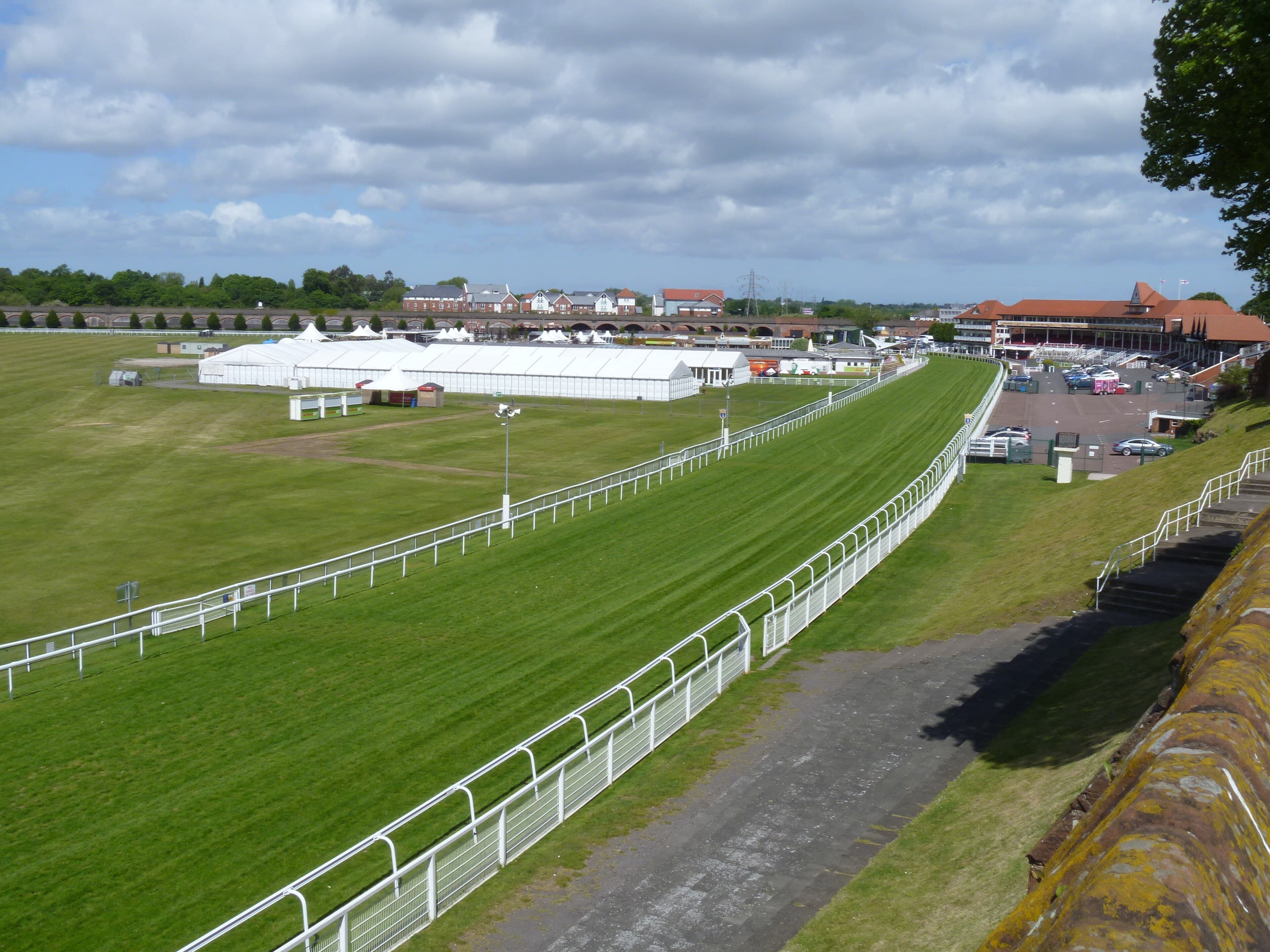 Chester racecourse from the city walls in late spring, the rail curving round towards the grandstand with hospitality marquees ranged across the centre.