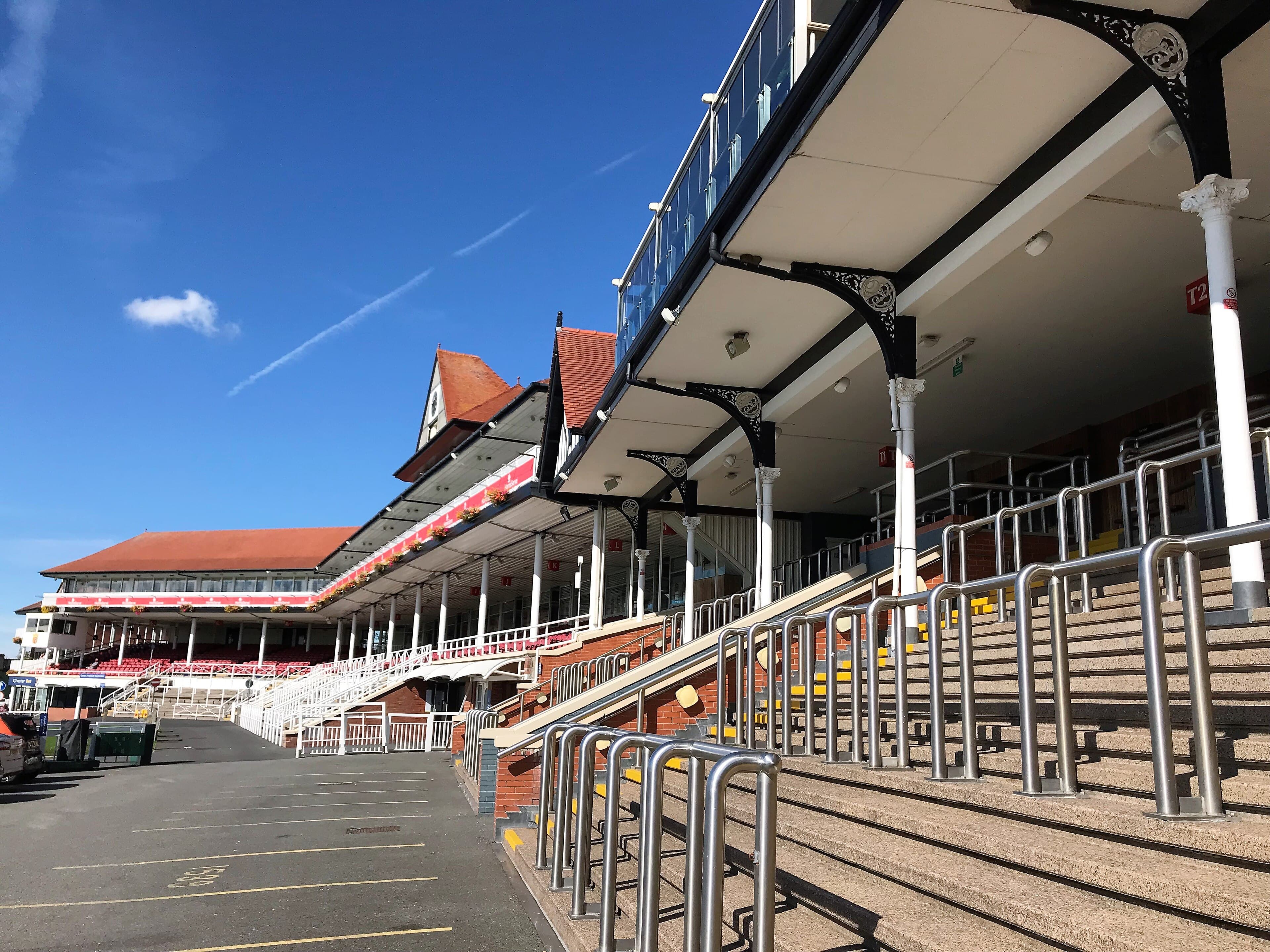 The County Stand at Chester racecourse from the walkway below, showing the Victorian ironwork canopy, the tiers of red seats and the clock tower.