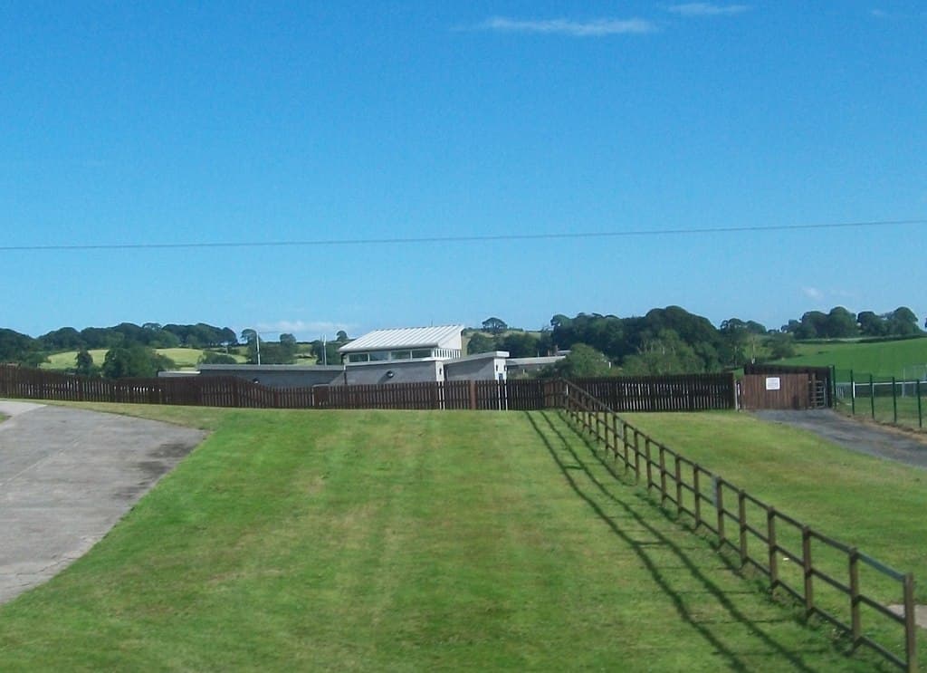 The low white buildings of Downpatrick racecourse across the turf under a clear blue sky.