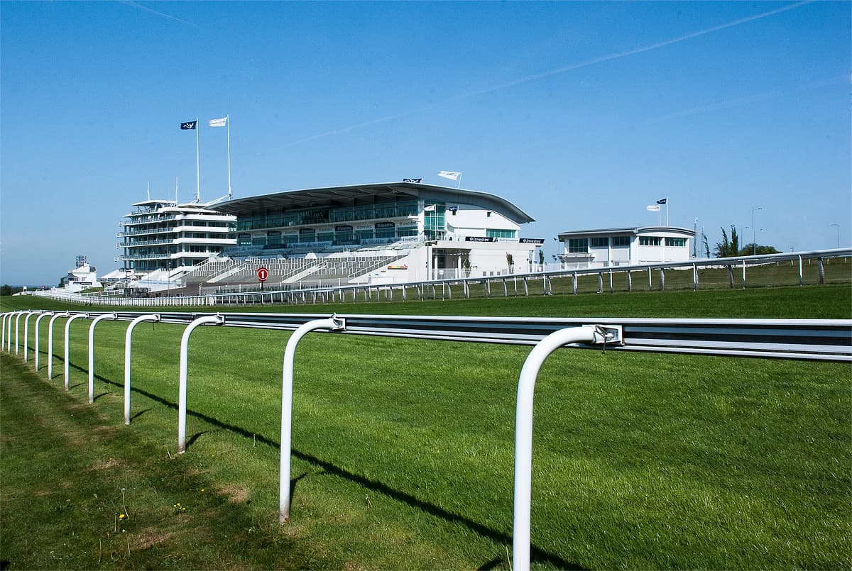 The Epsom grandstand and the running rail on a clear summer day, the turf mown in stripes.