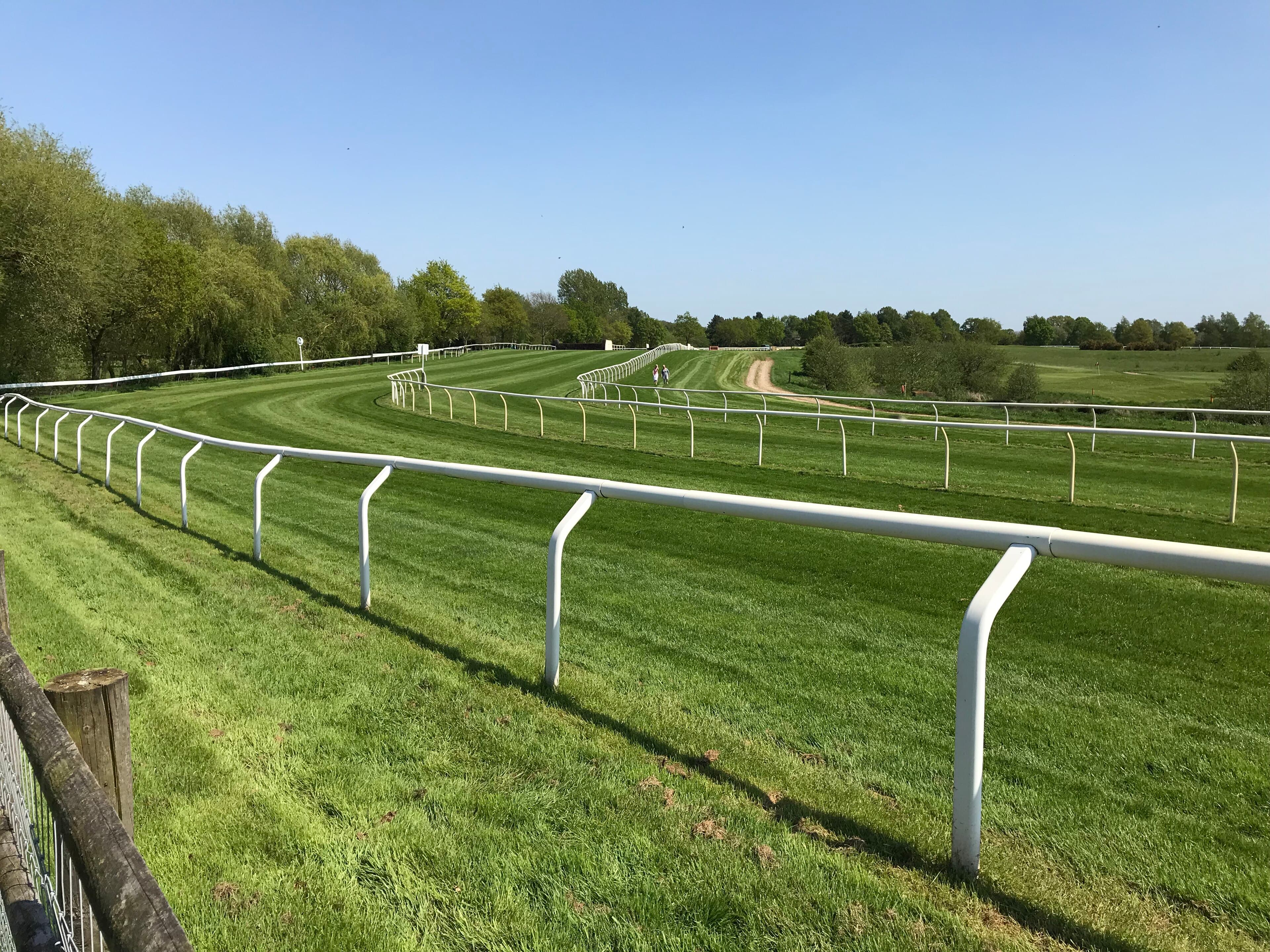 The final bend at Fakenham on a sunny spring morning, the white running rail curving away over closely mown turf with trees along the far side.