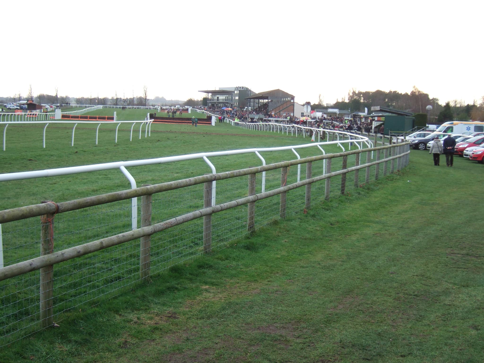 Looking along the finishing straight at Fakenham from behind the outside fence, with runners and the grandstands in the distance.