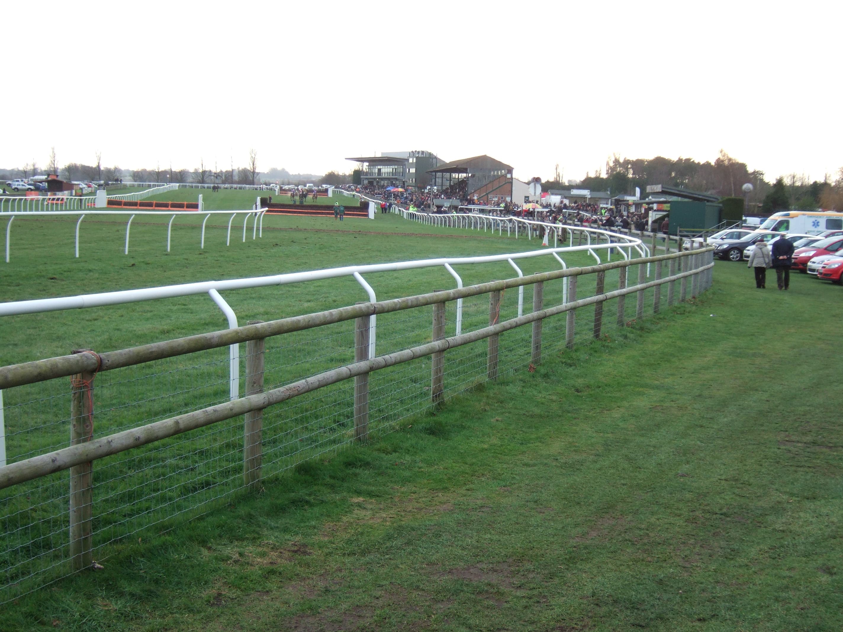 Looking along the finishing straight at Fakenham from behind the outside fence, with runners and the grandstands in the distance.