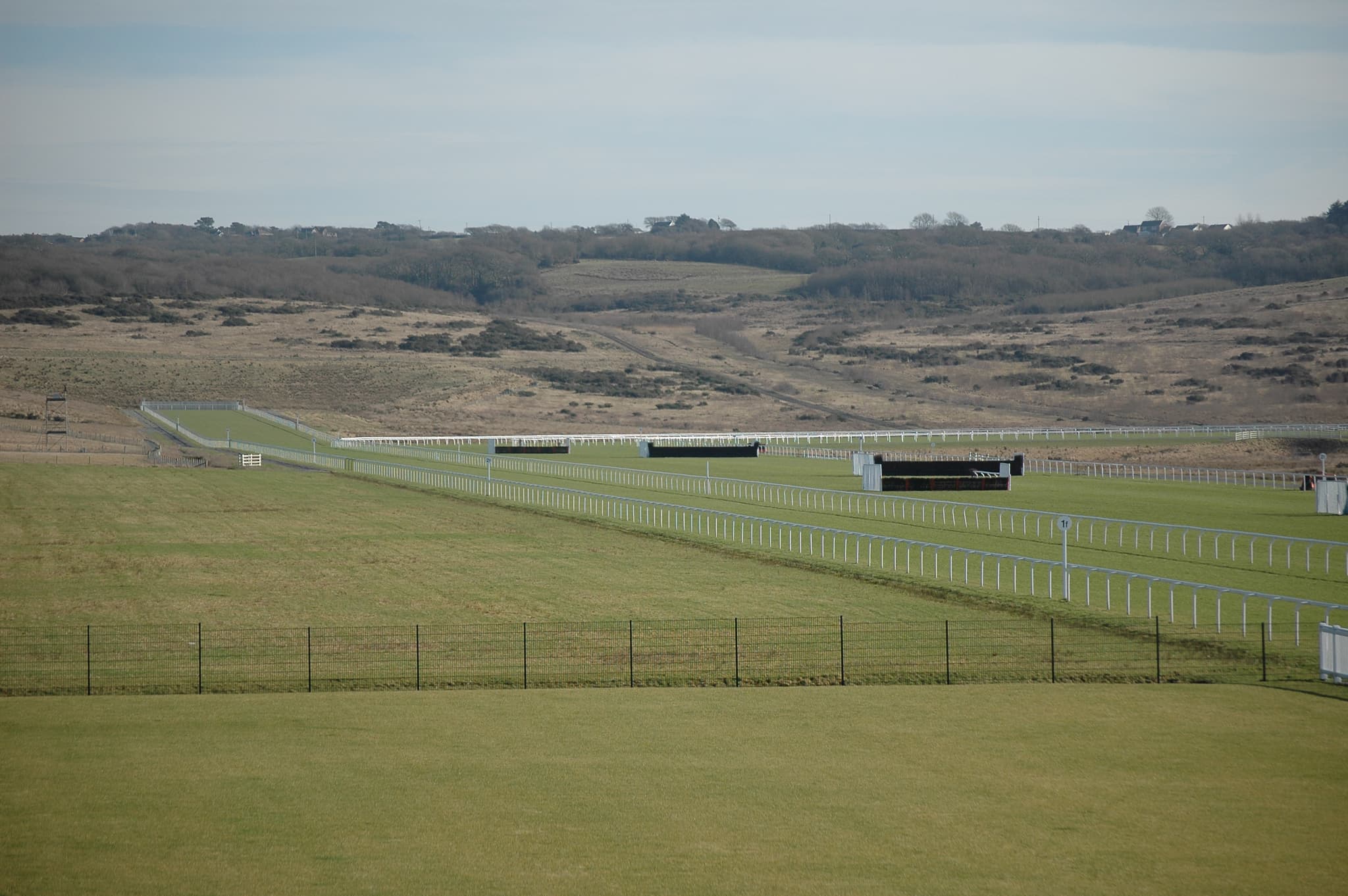 The rails and birch fences of Ffos Las racecourse laid out below the reclaimed hillside of the old opencast site.