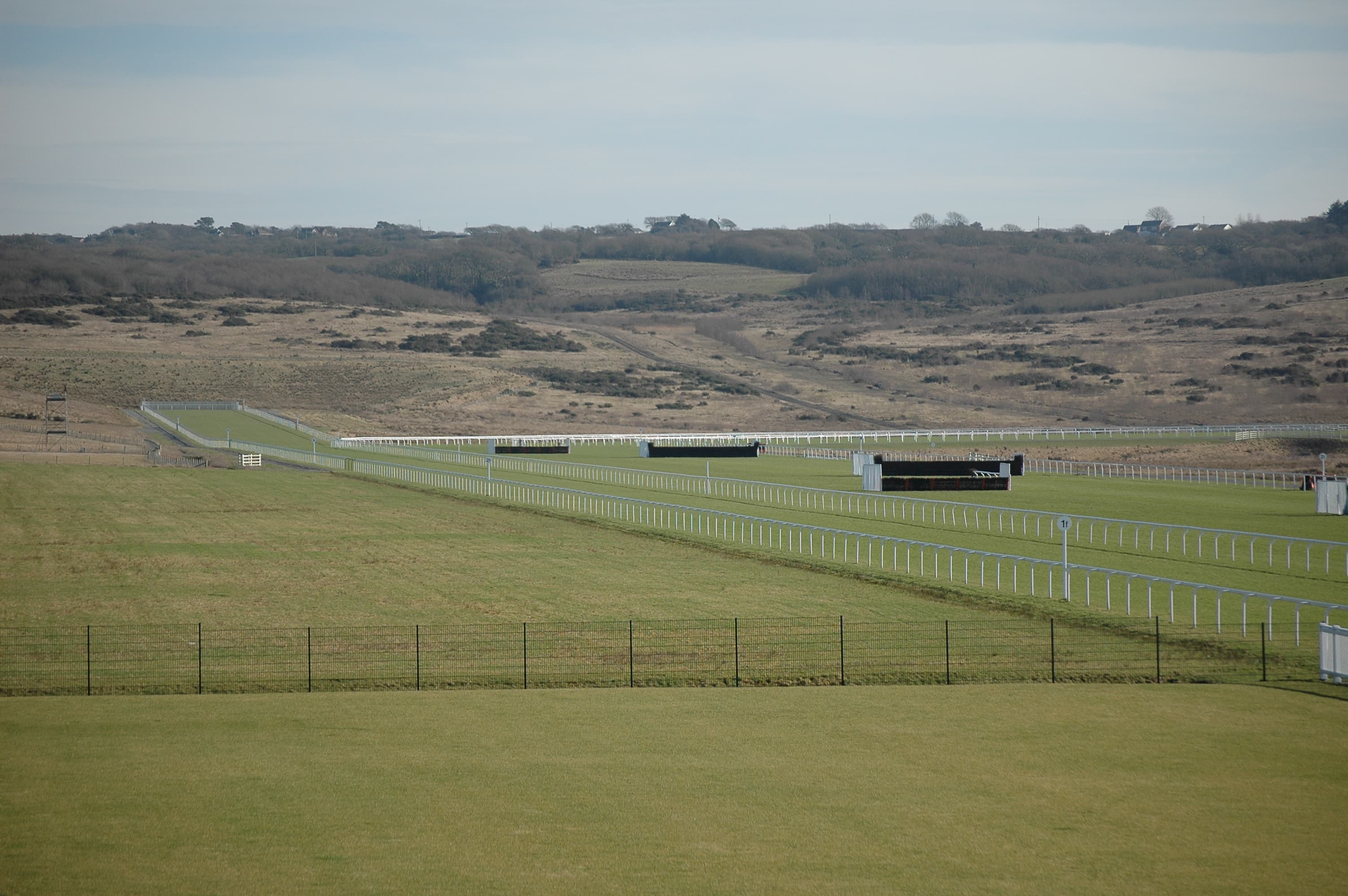 The rails and birch fences of Ffos Las racecourse laid out below the reclaimed hillside of the old opencast site.