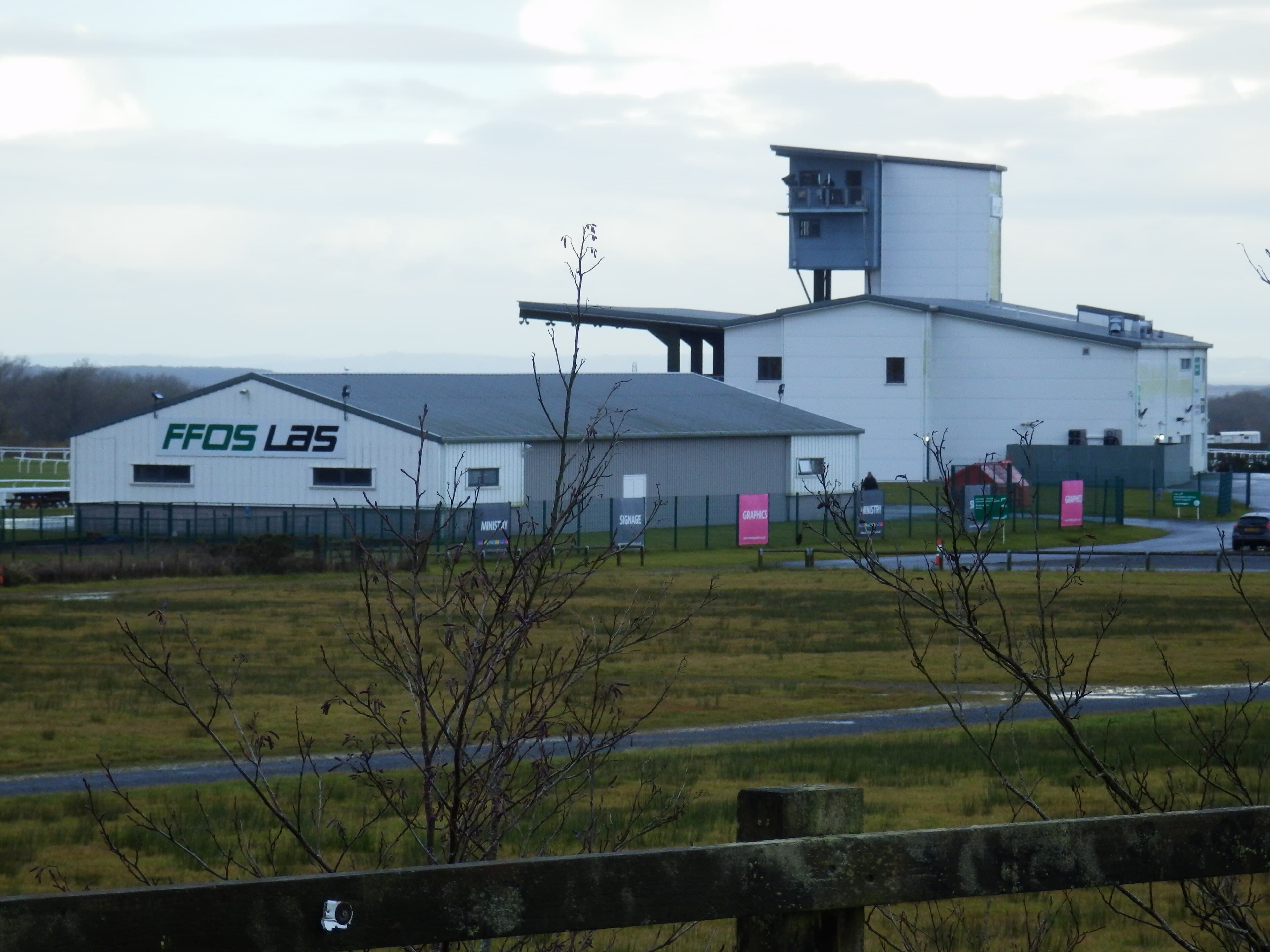 The main entrance building at Ffos Las racecourse, a long white shed with the course name across its end wall.