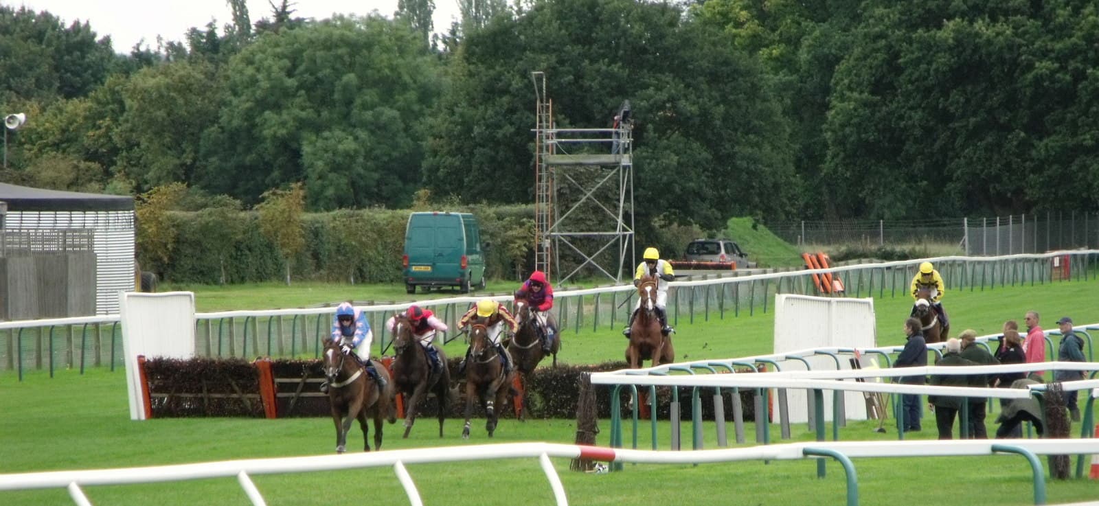 Four horses land over the last hurdle at Fontwell Park, with a fifth already clear up the running rail and a few spectators watching from the far side.