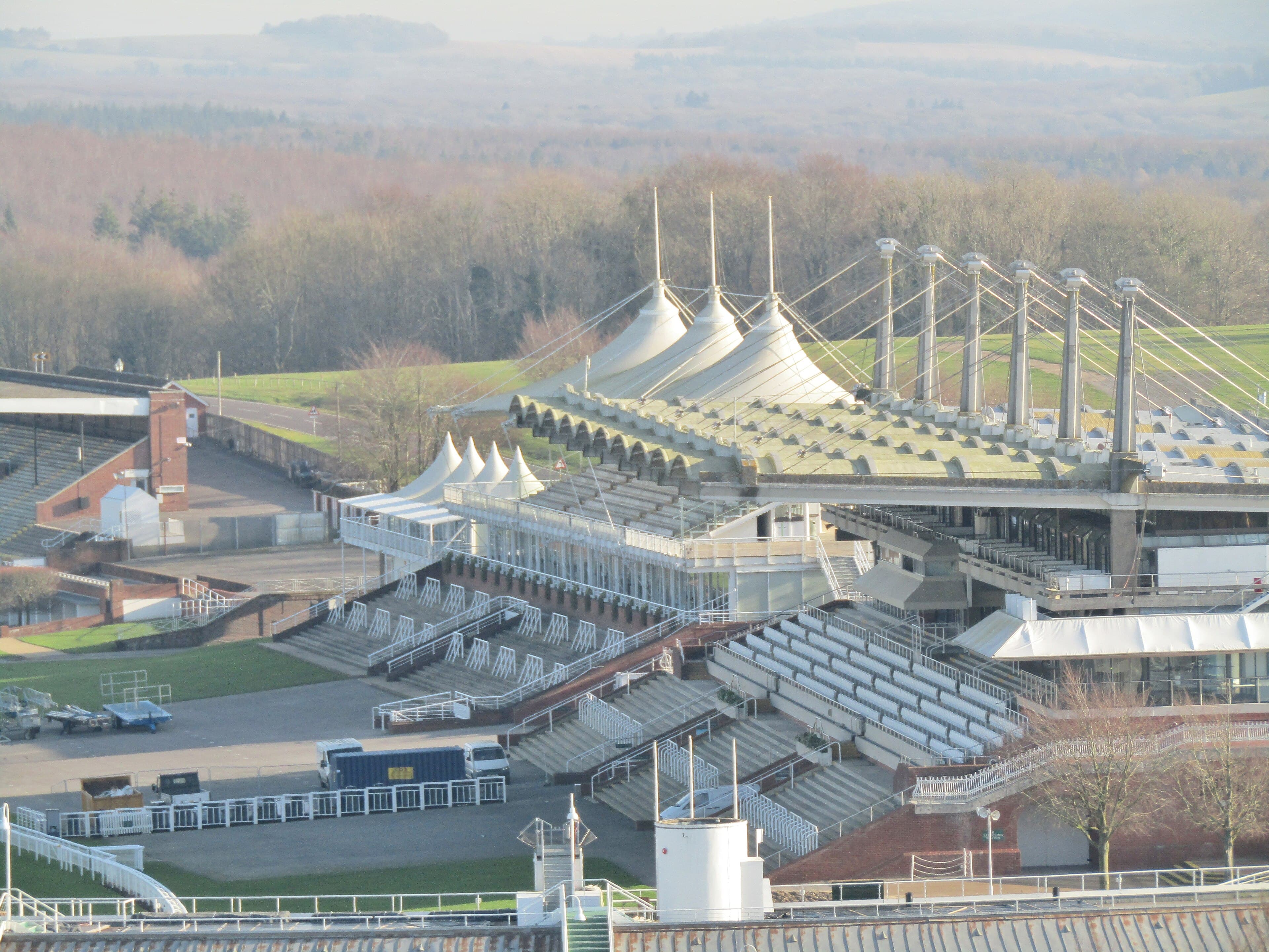 The sail canopy and terraces of the Goodwood grandstand seen from Trundle Hill in winter haze.
