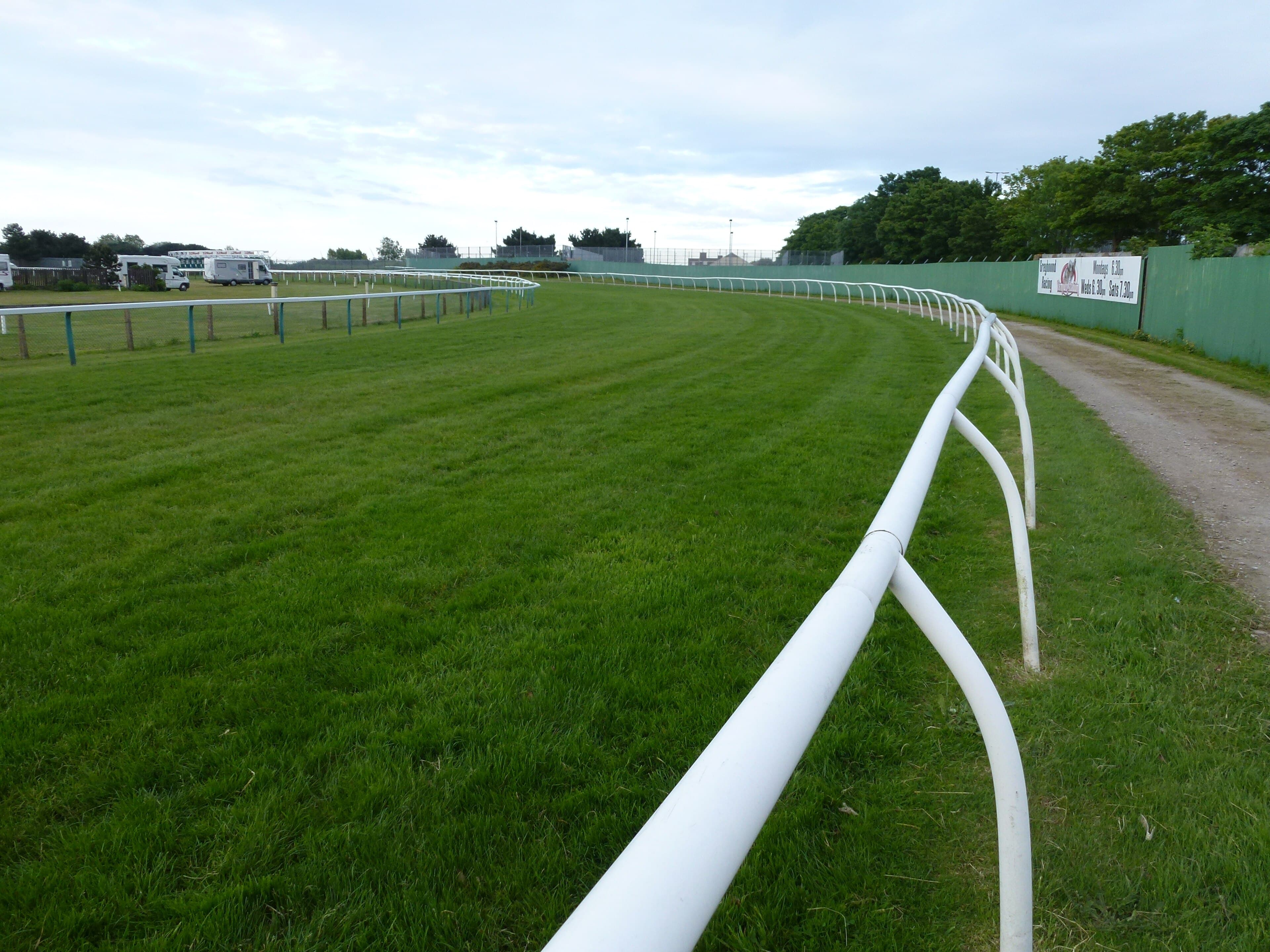 The running rail sweeping round a bend at Great Yarmouth racecourse, close-mown turf on the inside and a sandy walkway and green hoarding on the outside