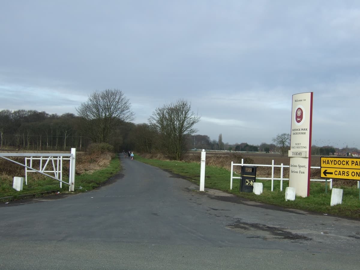 The Welcome to Haydock Park Racecourse board at the lane entrance, the course visible beyond the trees.
