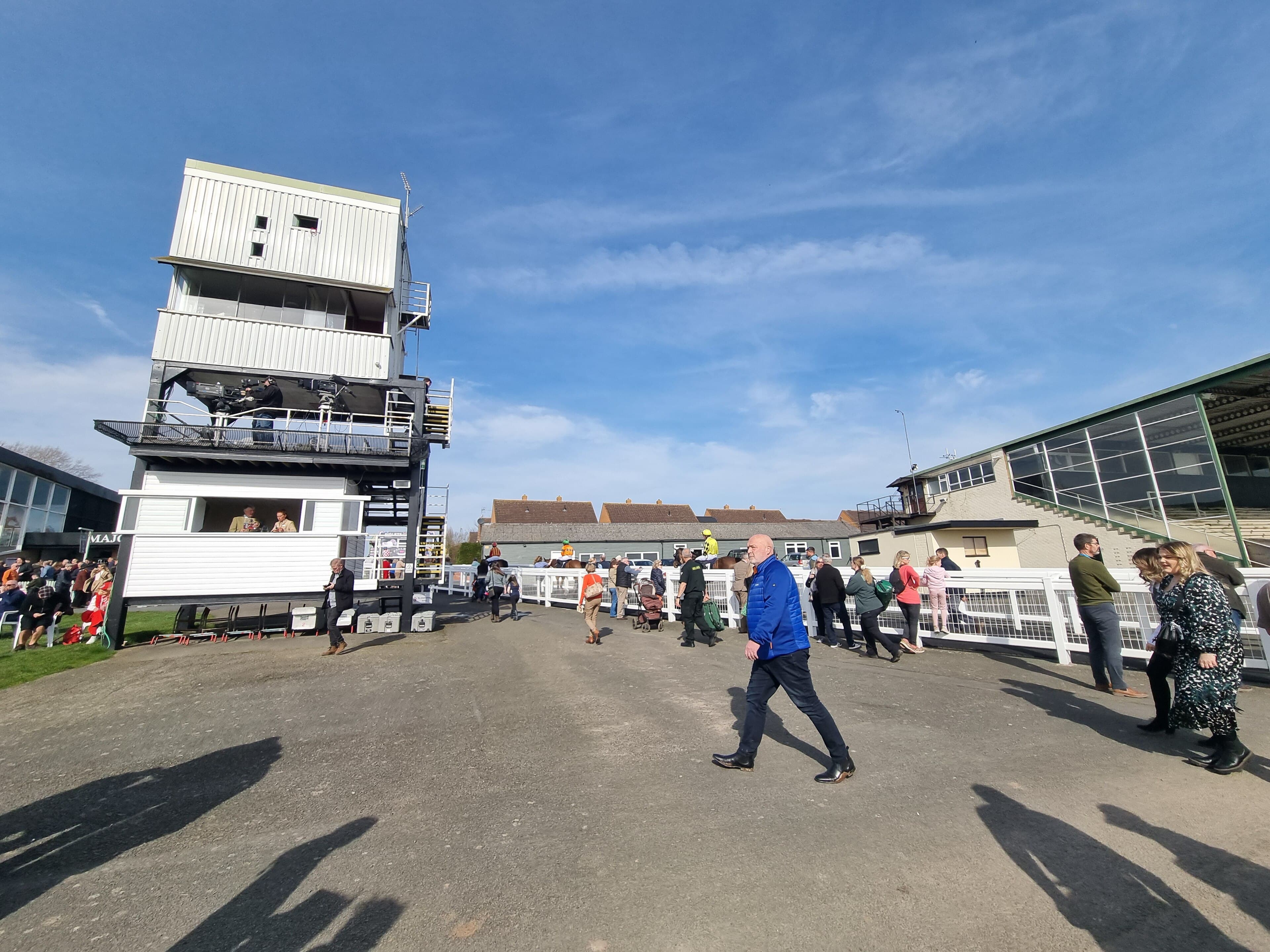 The white stewards' and commentary tower at Hereford with television cameras on its gantry, racegoers along the rail and the glass-fronted stand to the right.