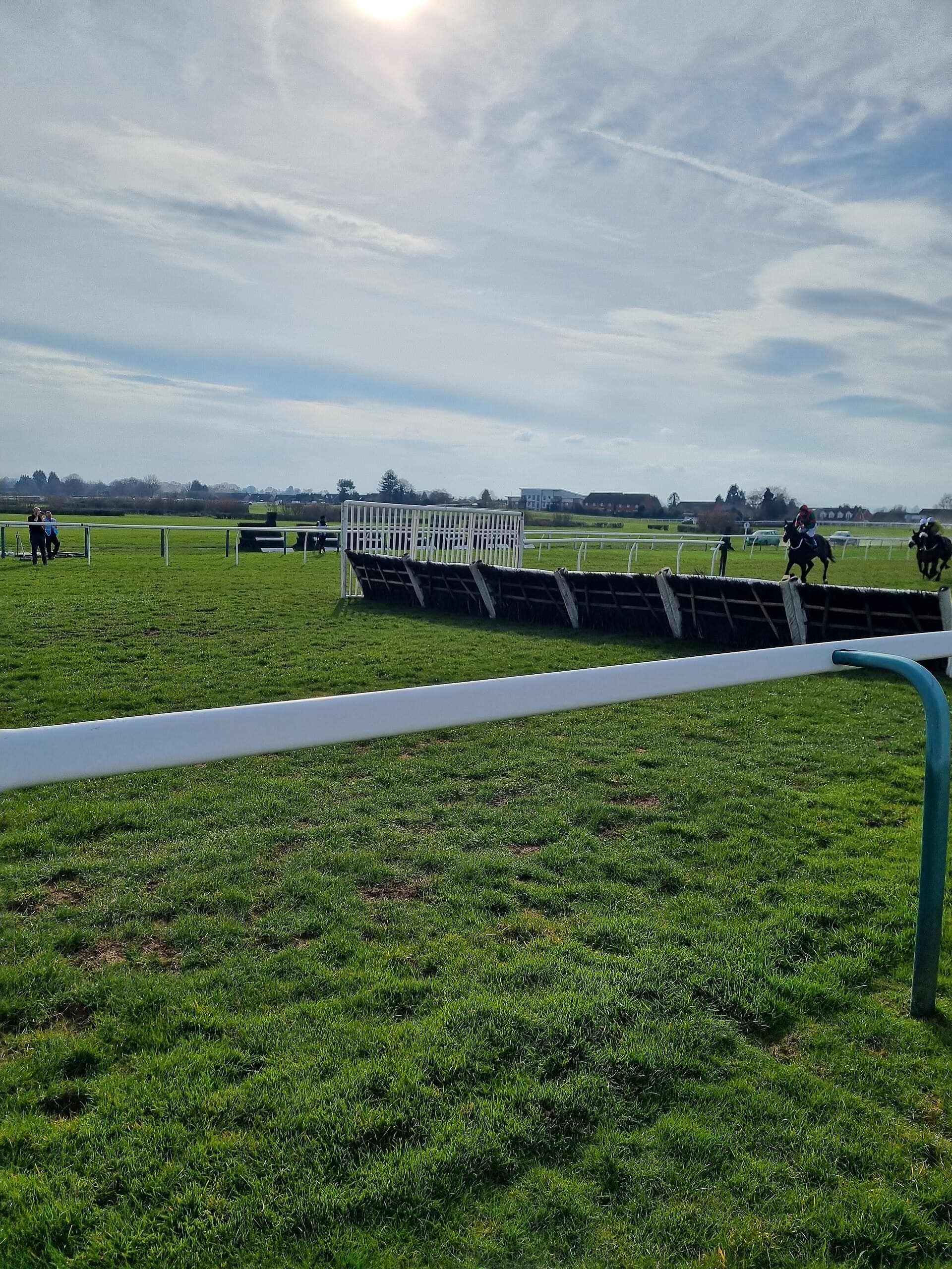 A plain birch hurdle with its white wing standing across the Hereford turf, a single horse jumping it at the far end and the far rail beyond.