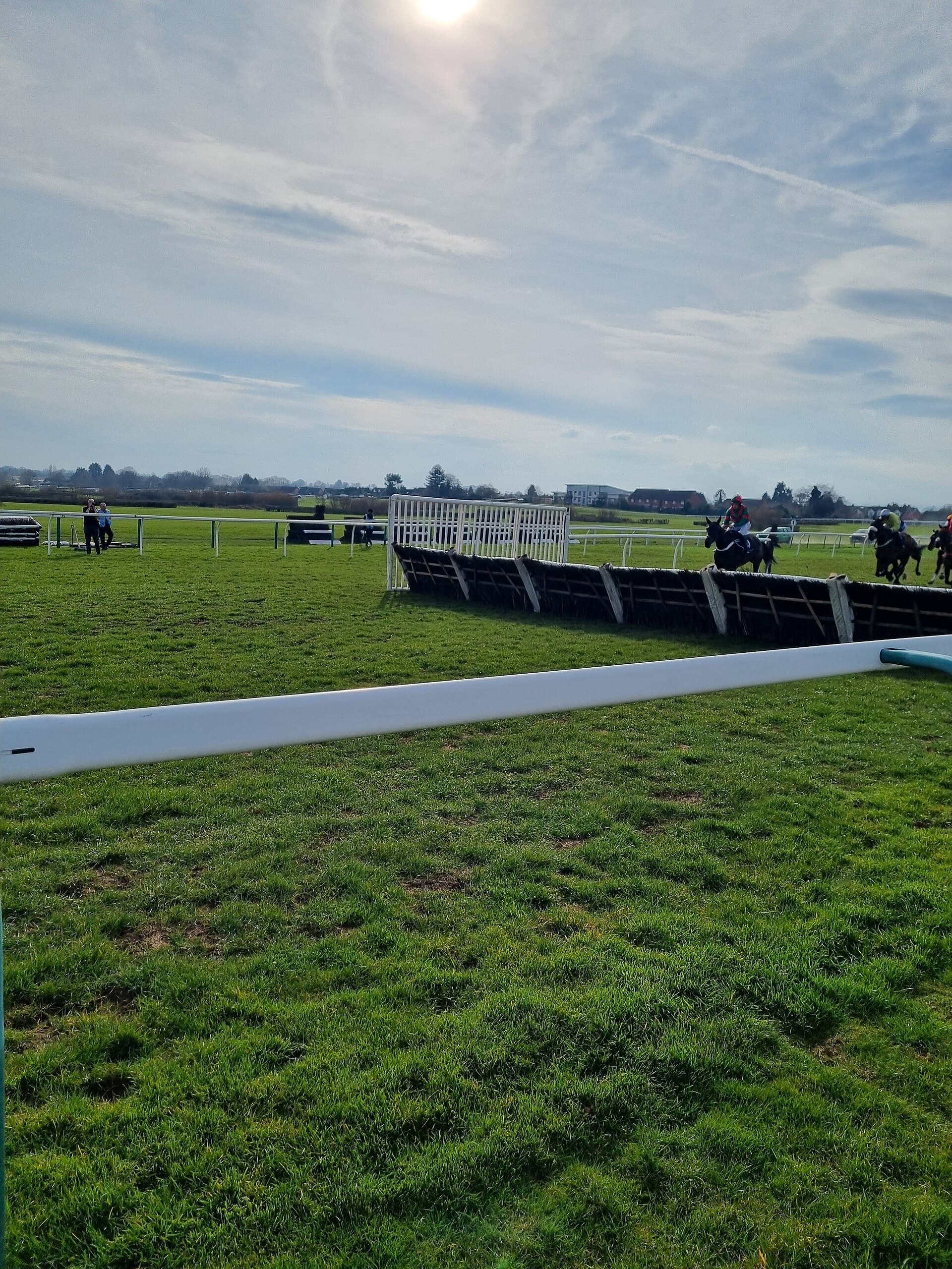 The hurdle line at Hereford with its white wing, a horse jumping at the far end and the rest of the field strung out along the back straight.
