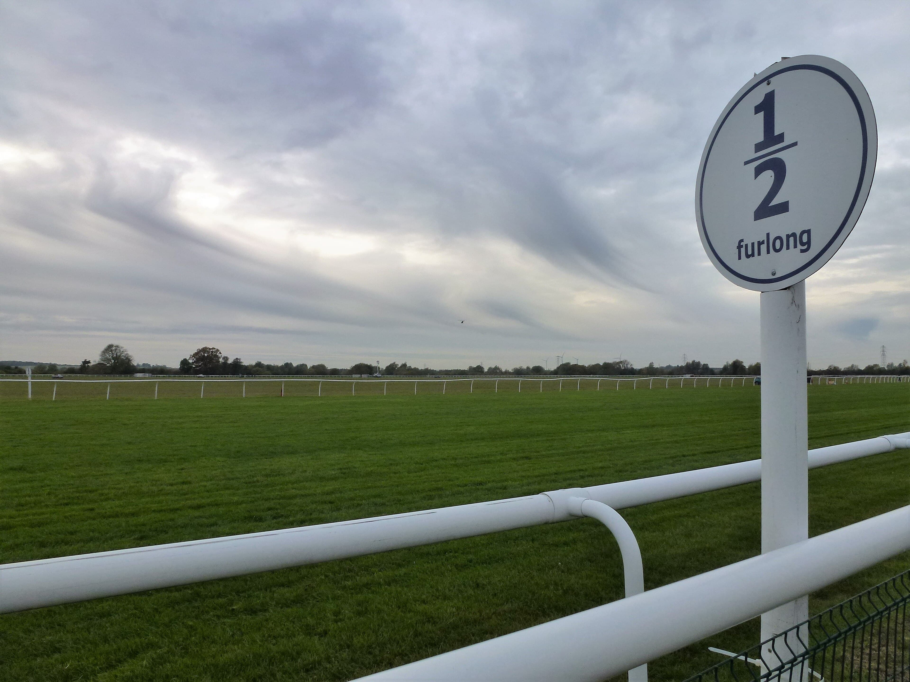 The half furlong marker post beside the white running rail at Huntingdon, the turf track running away flat under a grey sky