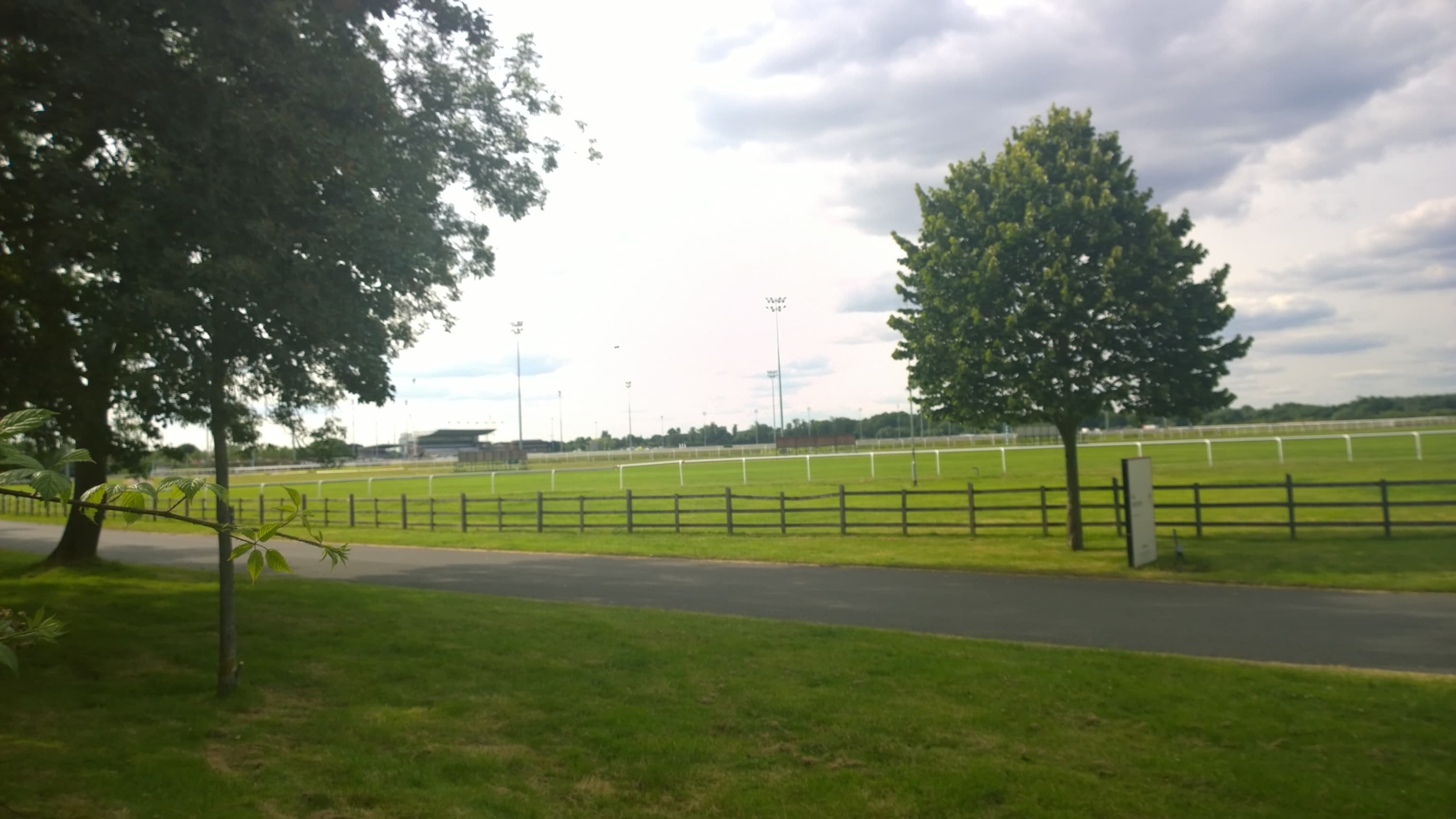 The turf course at Kempton Park beyond a post and rail fence, with the floodlights on the skyline.