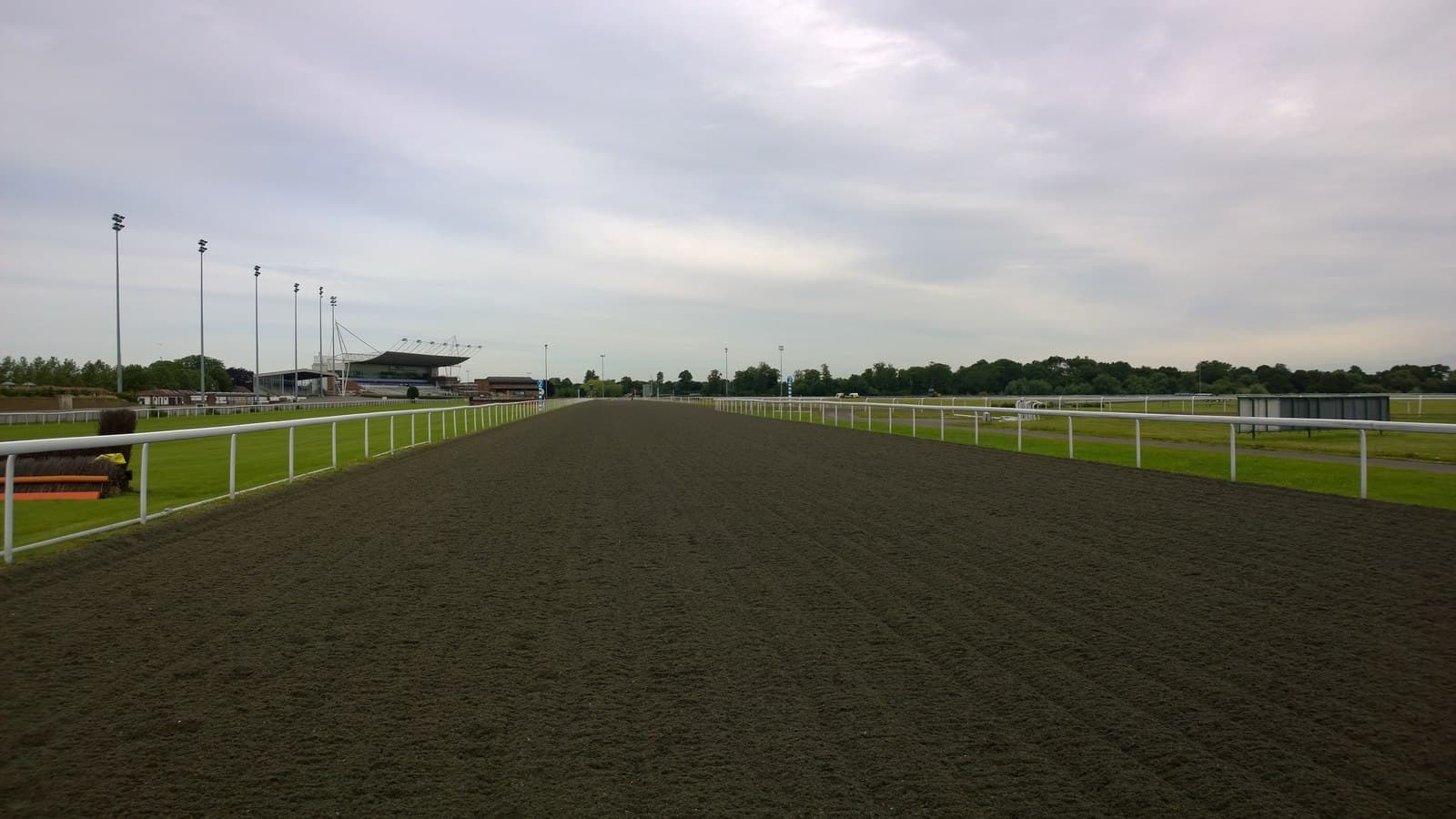 The all-weather main straight at Kempton Park running away towards the floodlights and the stand.