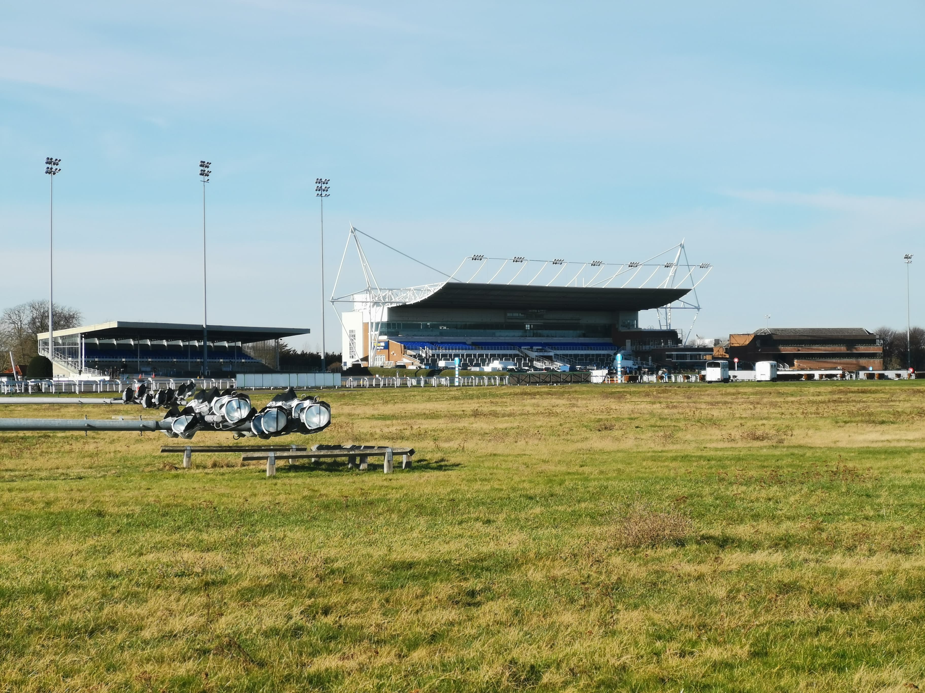The grandstand and floodlights at Kempton Park seen across the rough grass inside the course.
