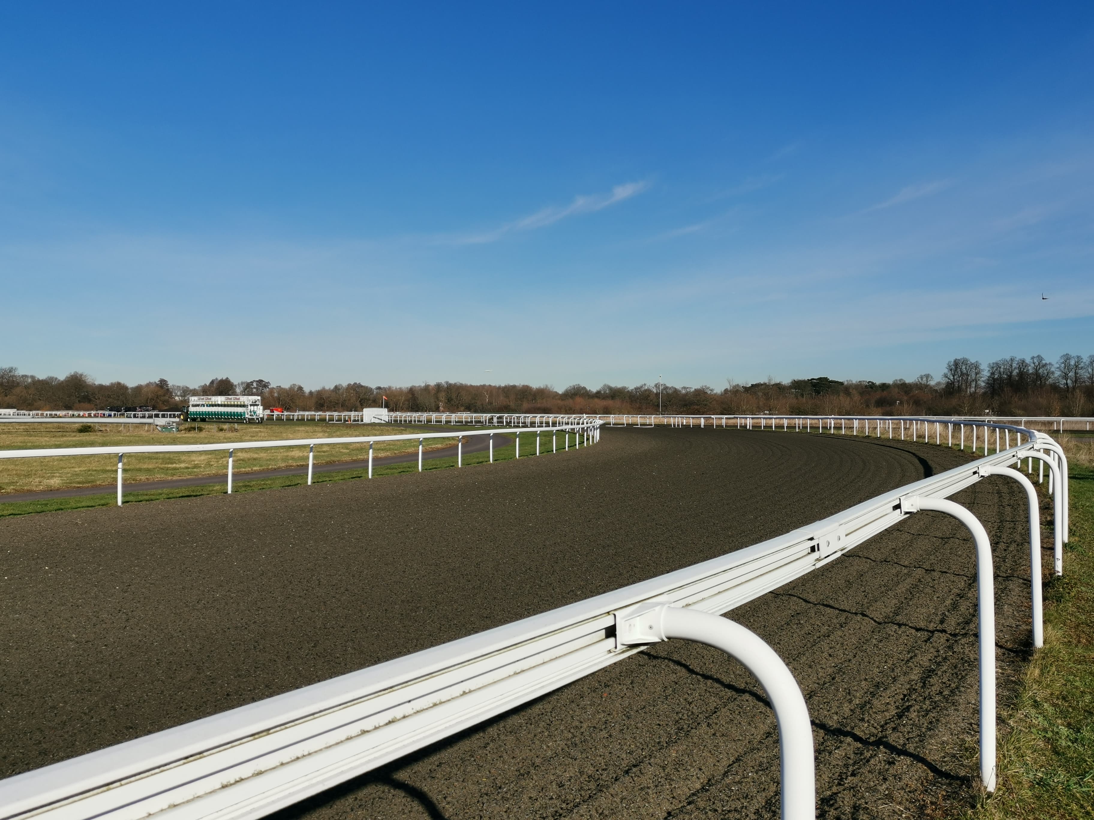 The Polytrack bend at Kempton Park sweeping round inside the white rail under a clear sky.