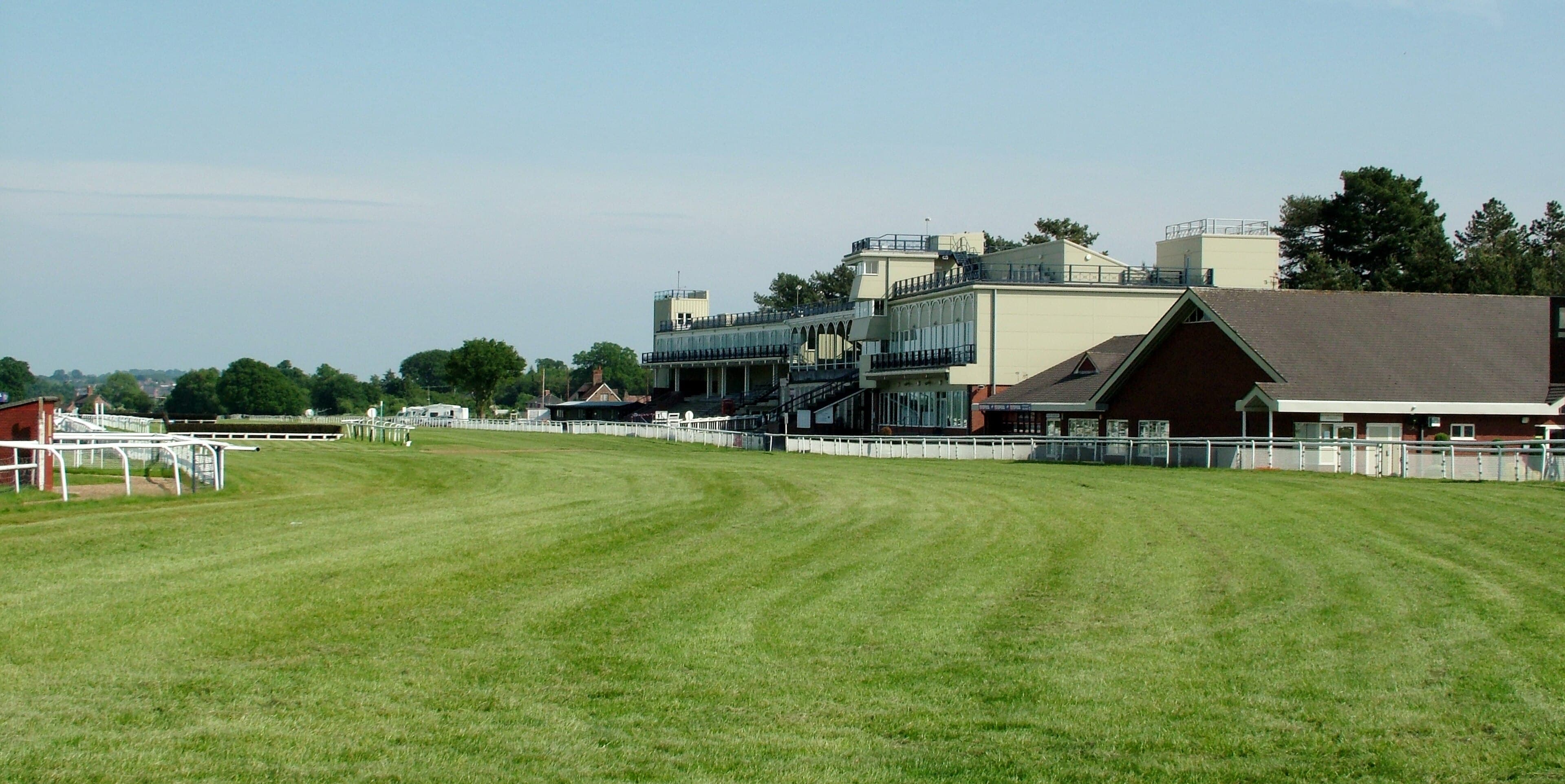 The grandstands at Ludlow Racecourse seen along the home straight, with the mown turf of the running strip in front of them on a bright summer day.