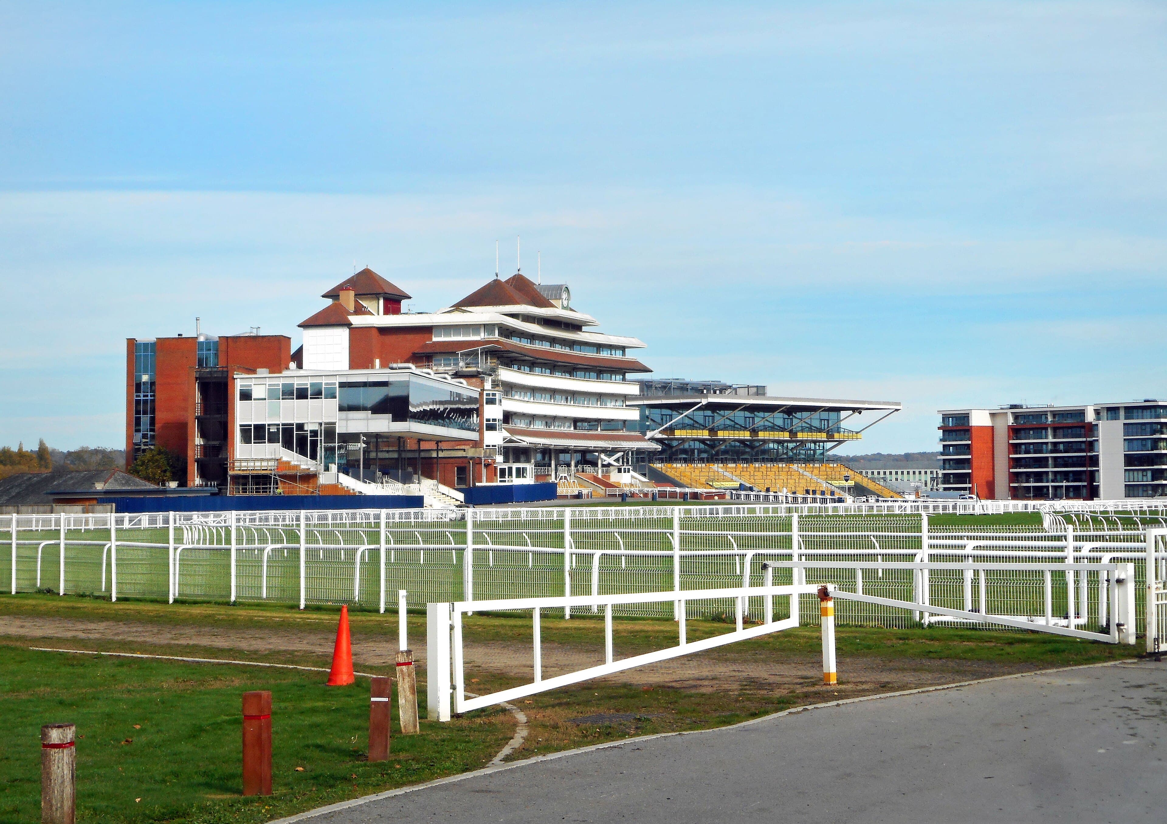 The Newbury stands from the racehorse crossing, white rails and gates in front under a blue autumn sky.