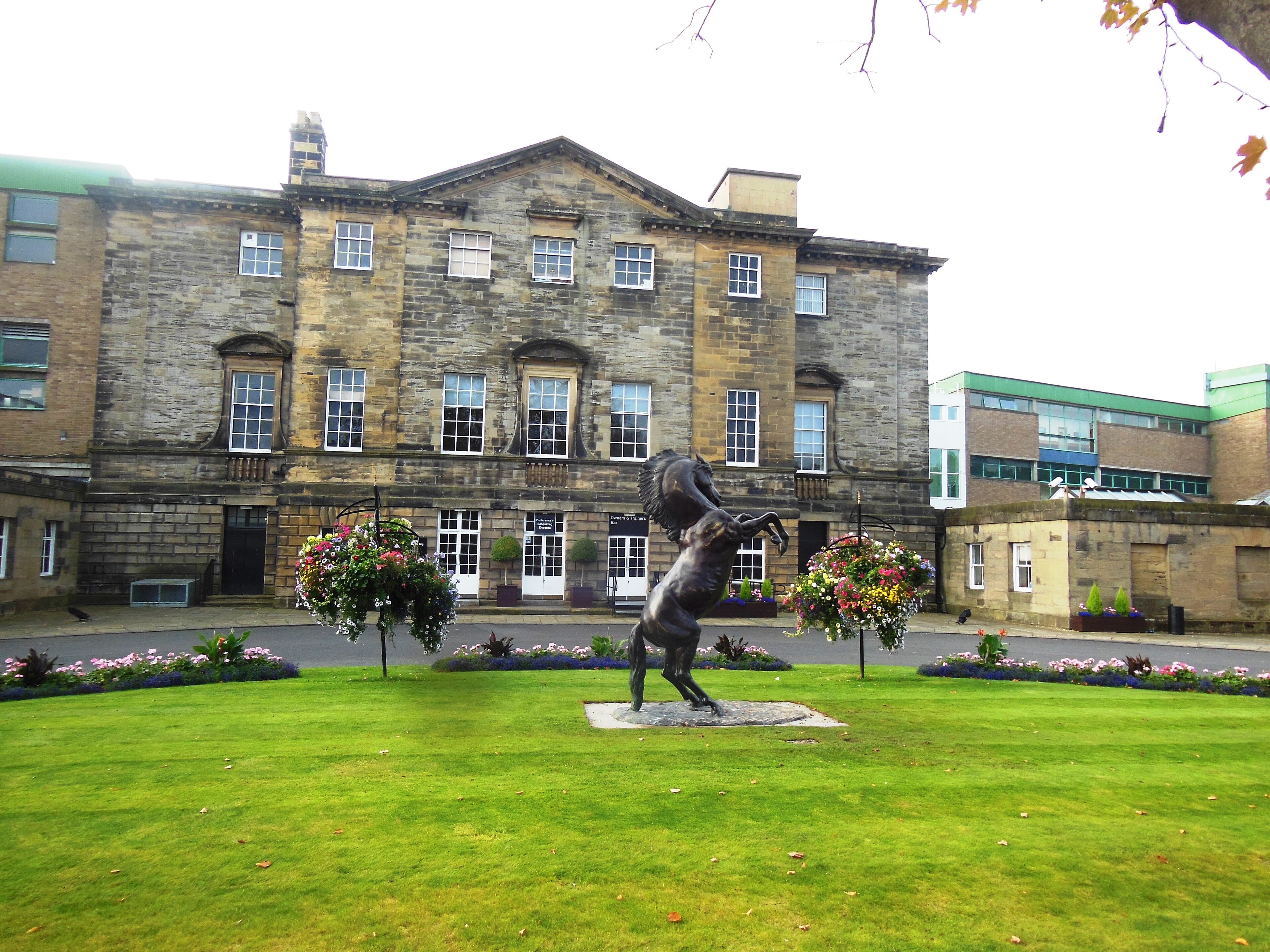 Brandling House at the entrance to Newcastle Racecourse, a bronze rearing horse on the lawn in front of the stone frontage.