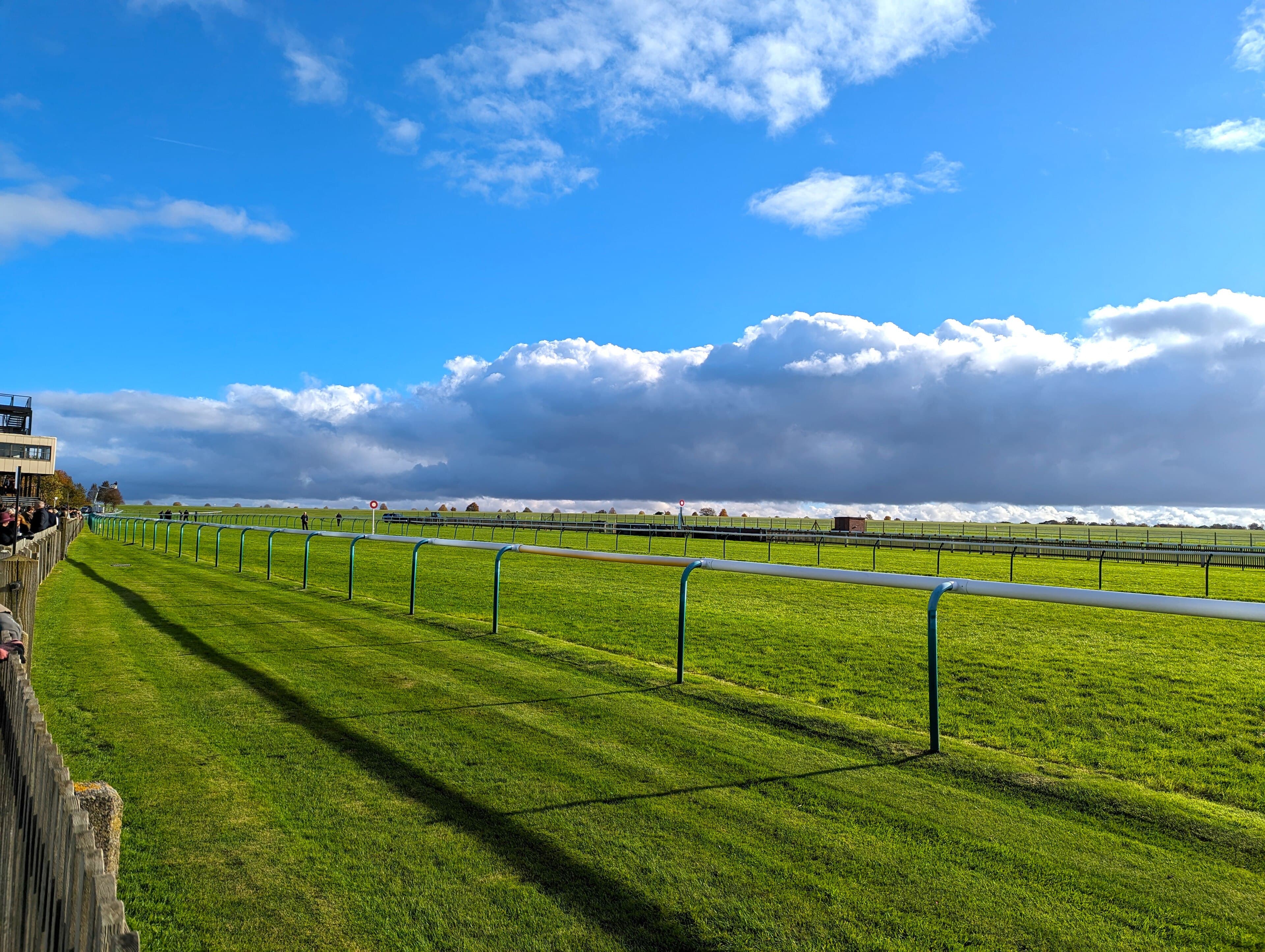 Storm cloud building over the Rowley Mile at Newmarket, the rail running away across the heath.