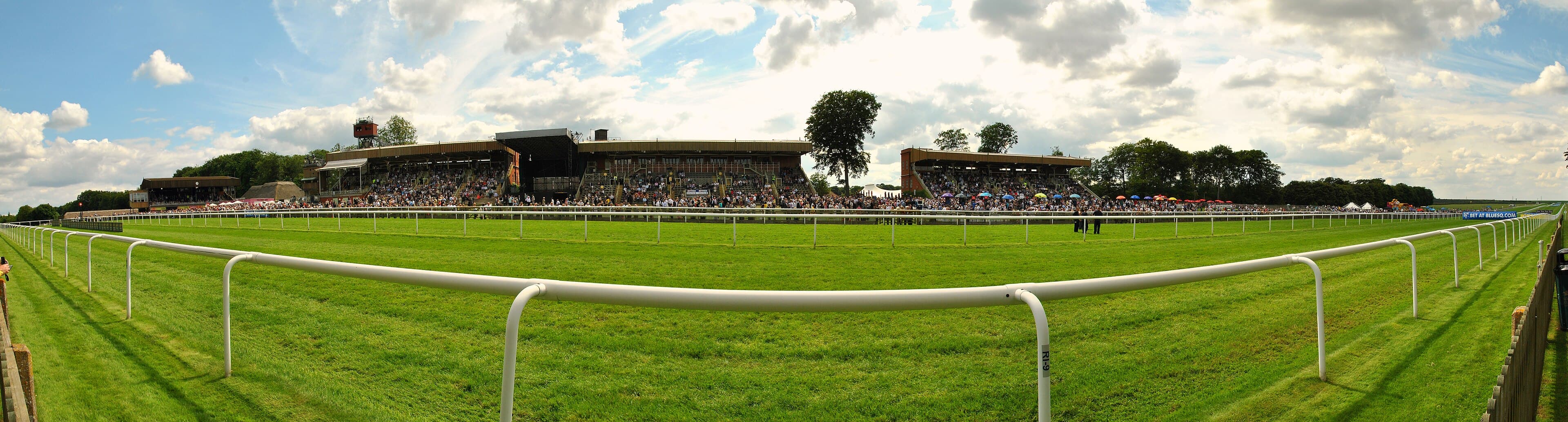 The thatched stands of Newmarket's July Course seen in panorama across the turf on a summer raceday.