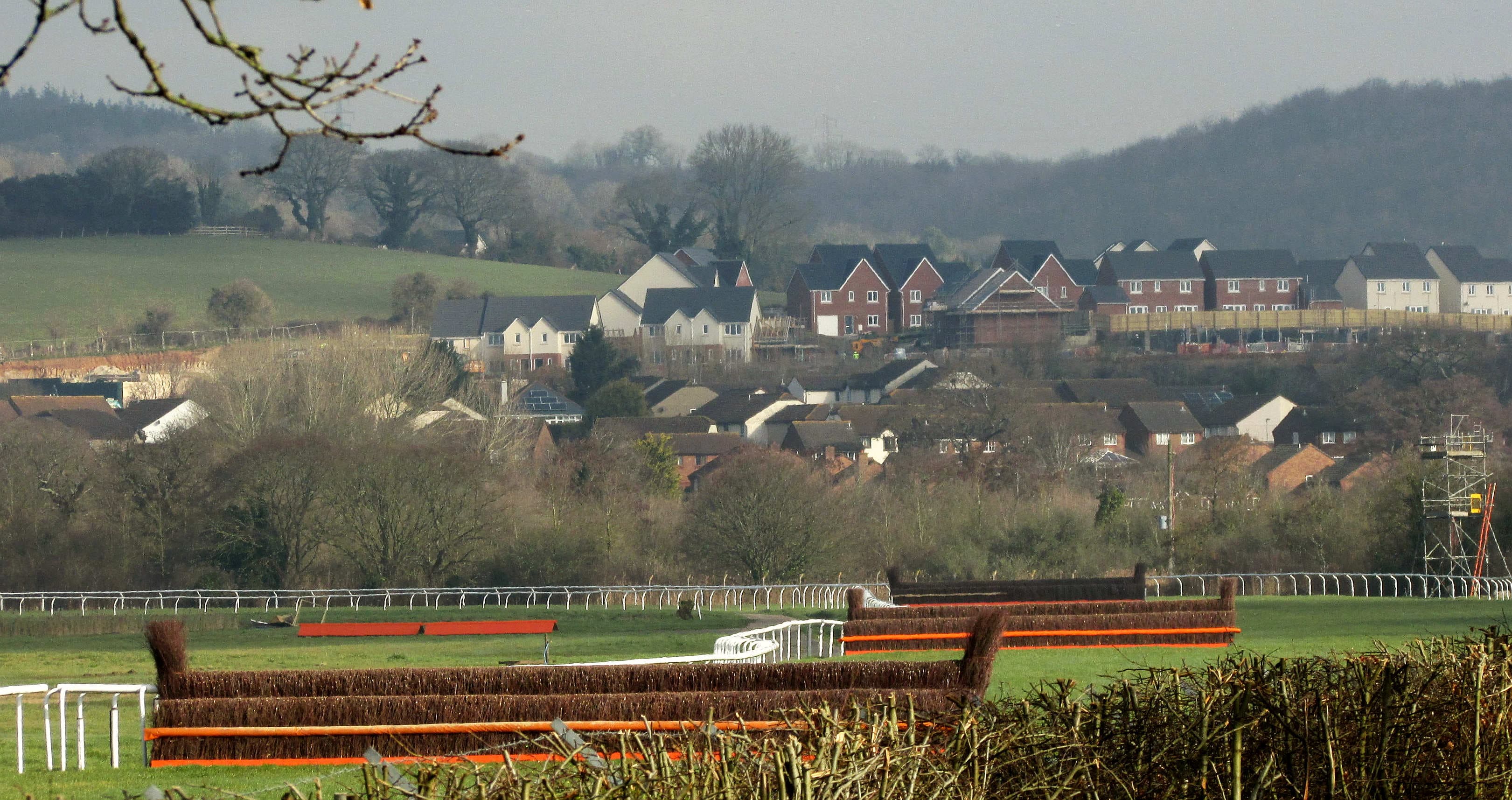 Two birch chase fences with orange take-off boards on the far side at Newton Abbot, the town and the hills of the Teign valley beyond.