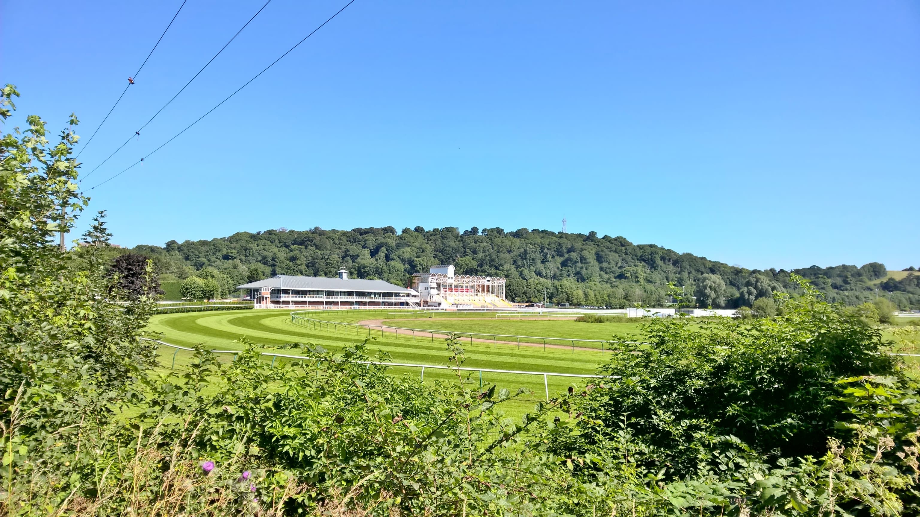 Nottingham Racecourse from the Colwick Wood side, the whole left-handed circuit and the white grandstand under a blue sky.