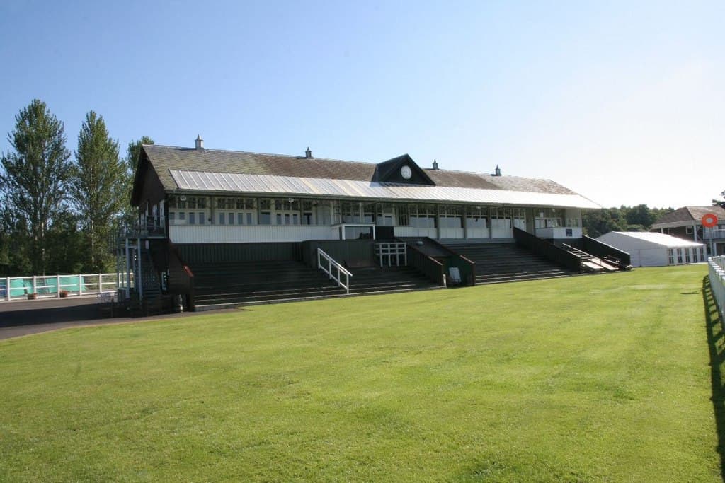 The long green-roofed stand at Perth racecourse seen across the turf on a clear day.