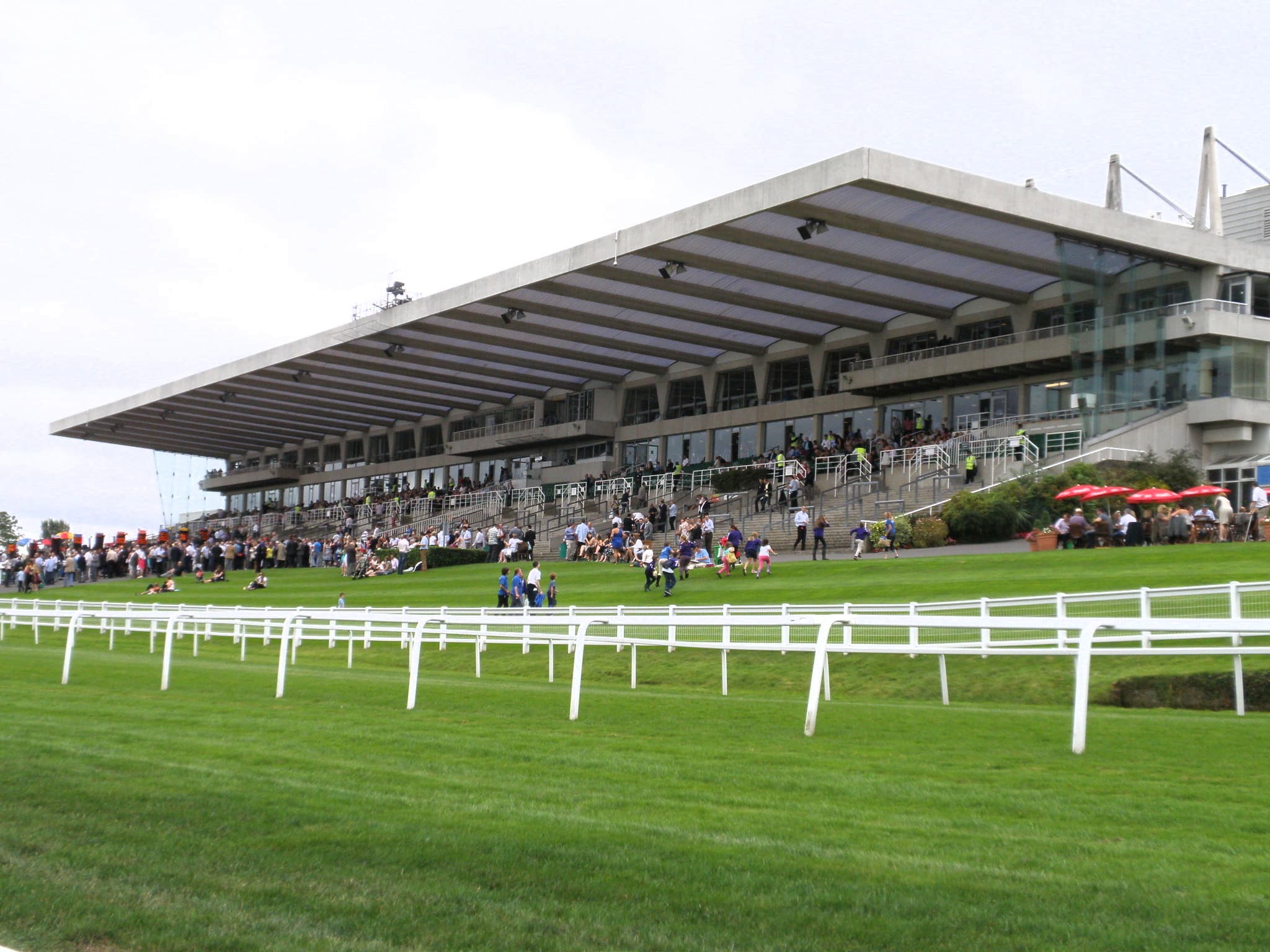 The cantilevered grandstand at Sandown Park above the rails, with racegoers spread along the lawn.