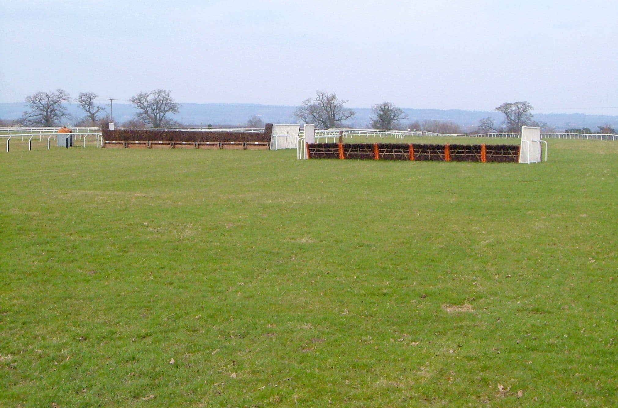 A hurdle and a chase fence side by side on the far side at Taunton, the Blackdown Hills on the skyline.