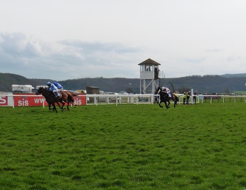 Two runners fighting out the finish at Taunton, a third horse well back and the judge's box beyond the rail.