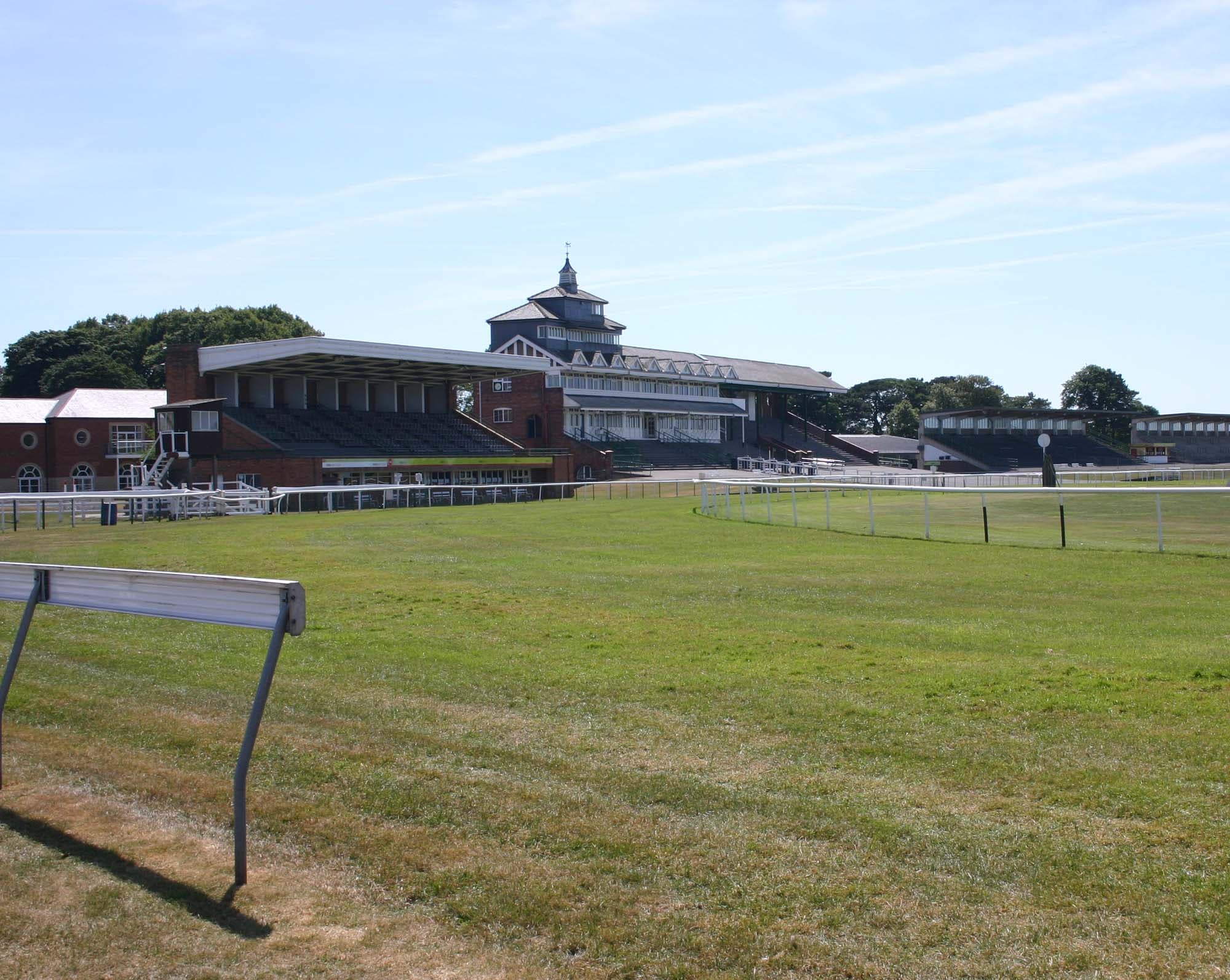 The stands at Thirsk Racecourse across the turf under a clear spring sky, the cupola of the old stand above the roof line.